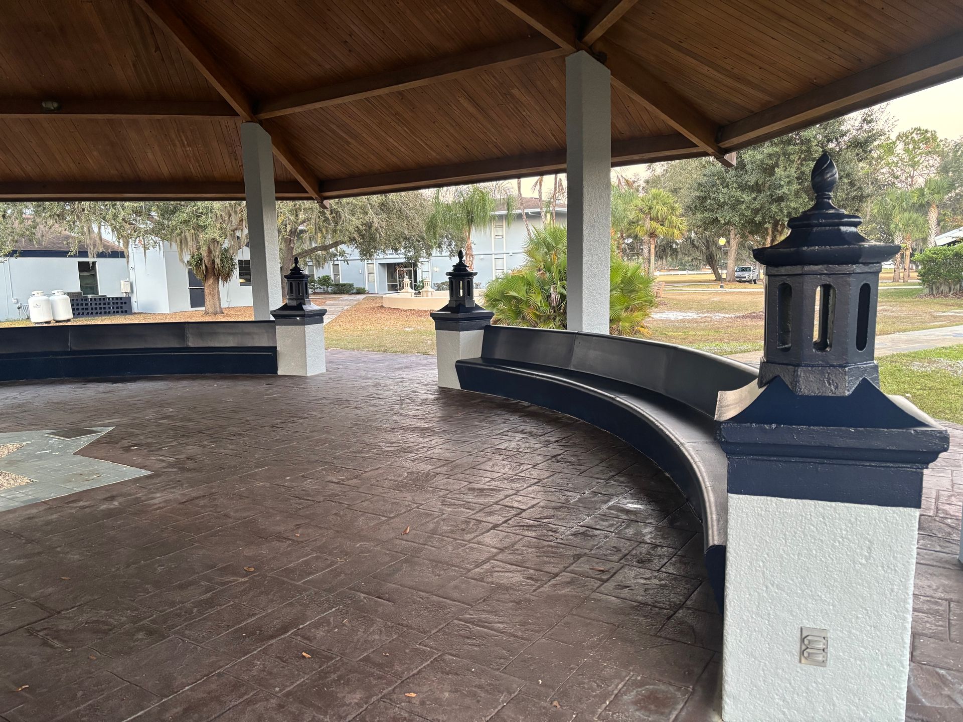 Gazebo with curved bench and dark blue accents, in a park.
