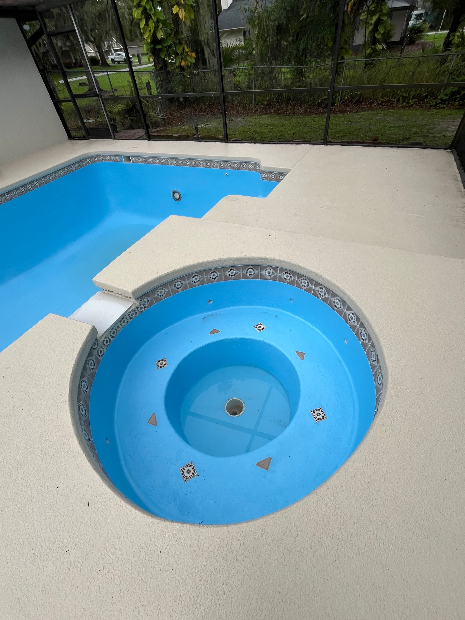 A blue pool and spa surrounded by light-colored concrete decking.