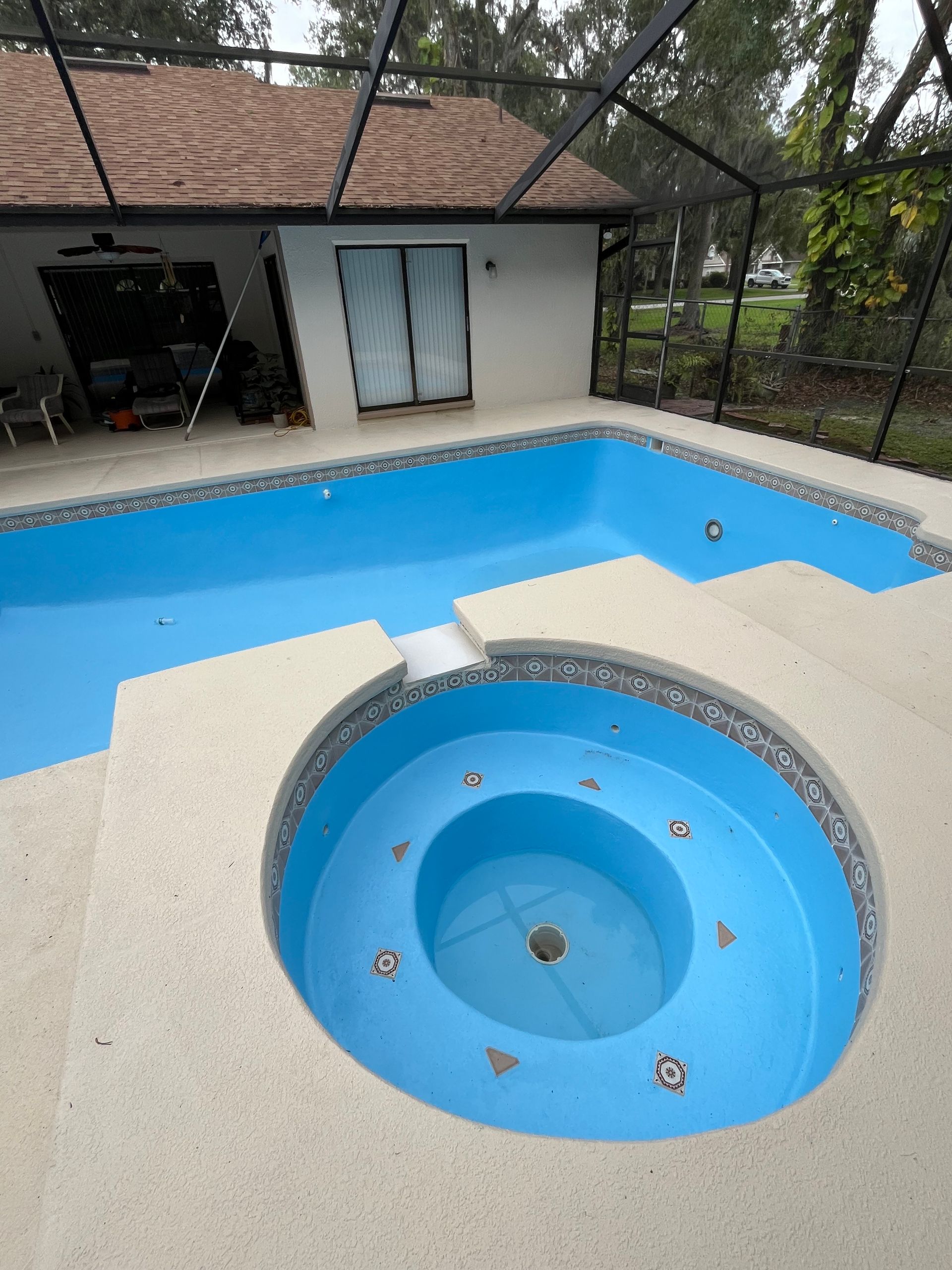 A freshly painted blue swimming pool with a connected spa. The pool and spa are set in a light-colored concrete patio.