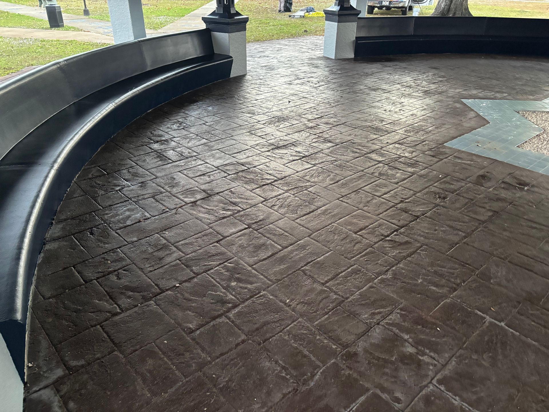 Gazebo interior with curved seating and textured brown concrete floor.