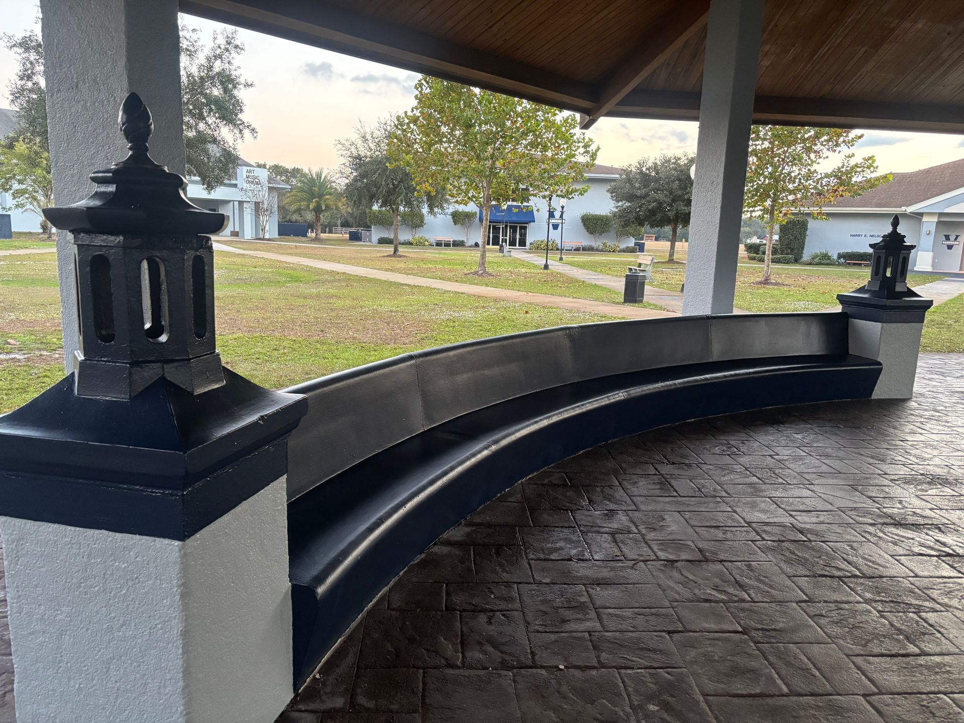 Curved bench under a gazebo with black and gray accents in a park.