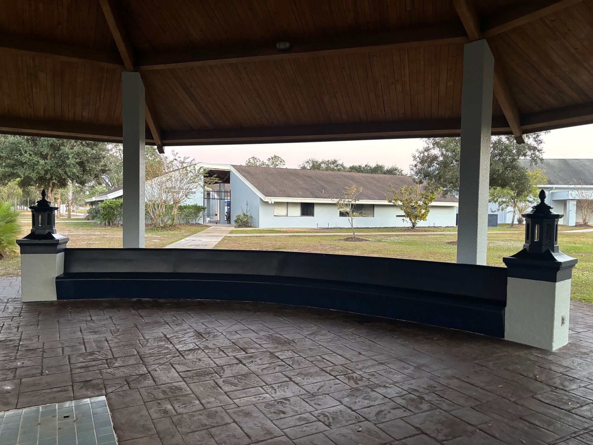 Gazebo with curved bench; view of buildings and lawn in the distance.