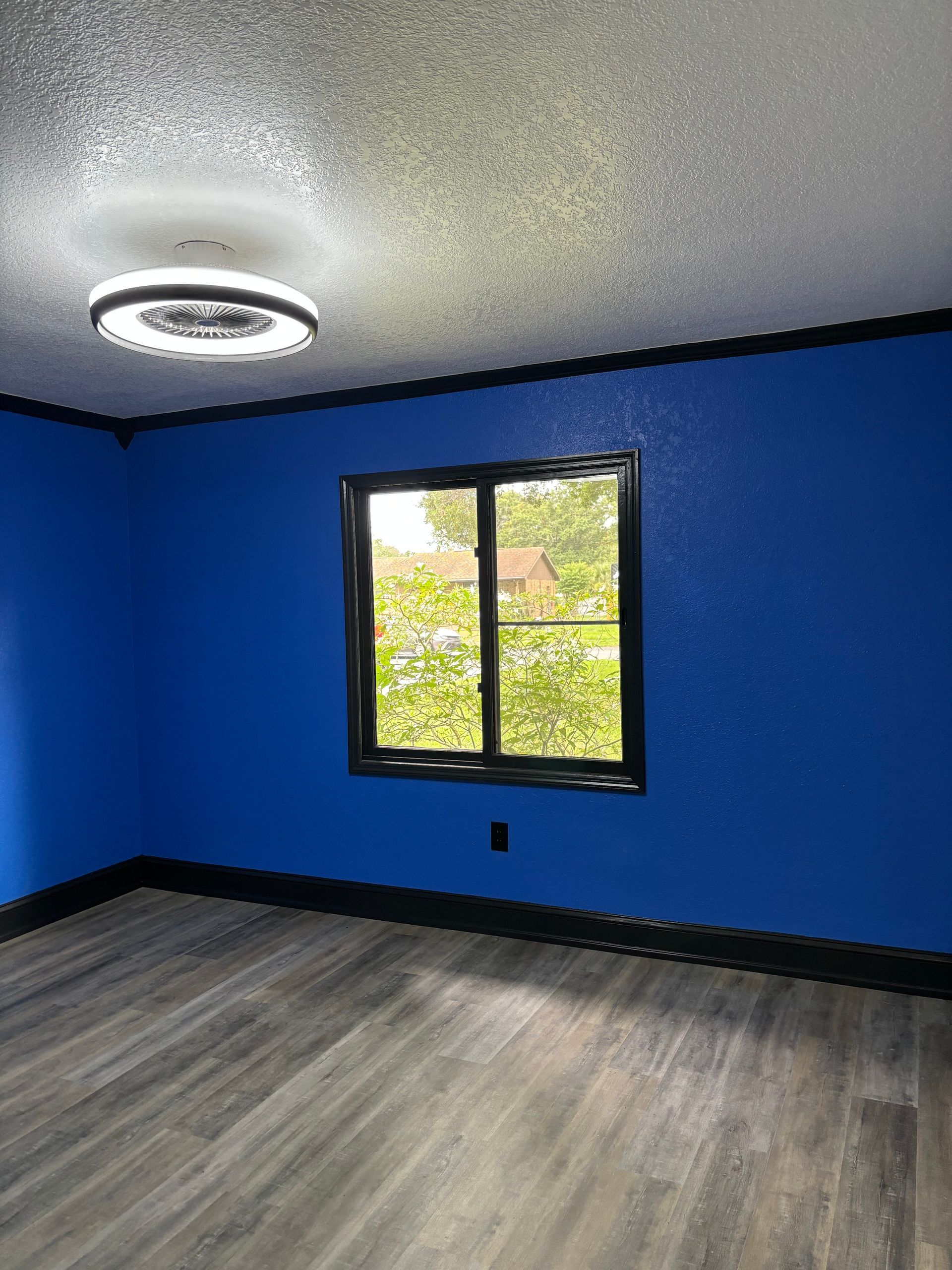 Blue room with black trim, a window, and gray wood-look flooring. A modern light fixture is on the ceiling.