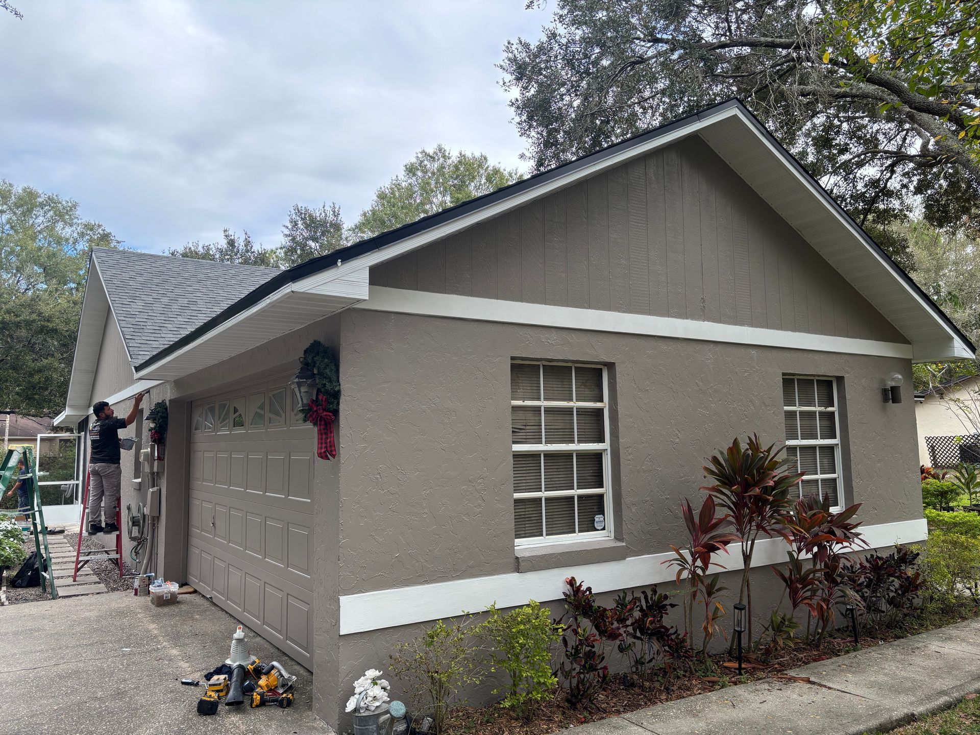 House exterior with a person painting trim. Gray stucco with white trim, gray garage door.
