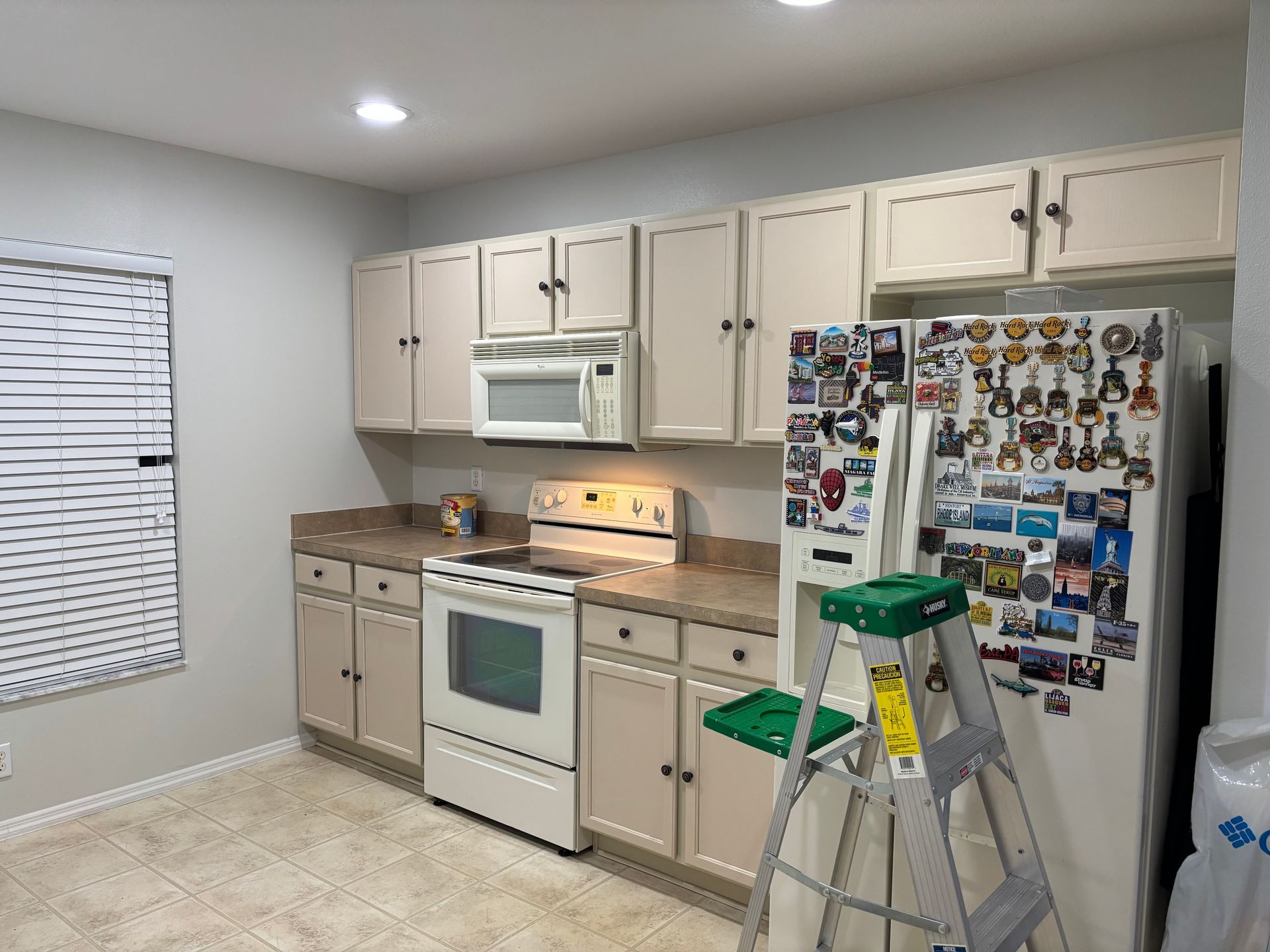 Kitchen with cream cabinets, white appliances, and a ladder by a refrigerator covered in magnets.