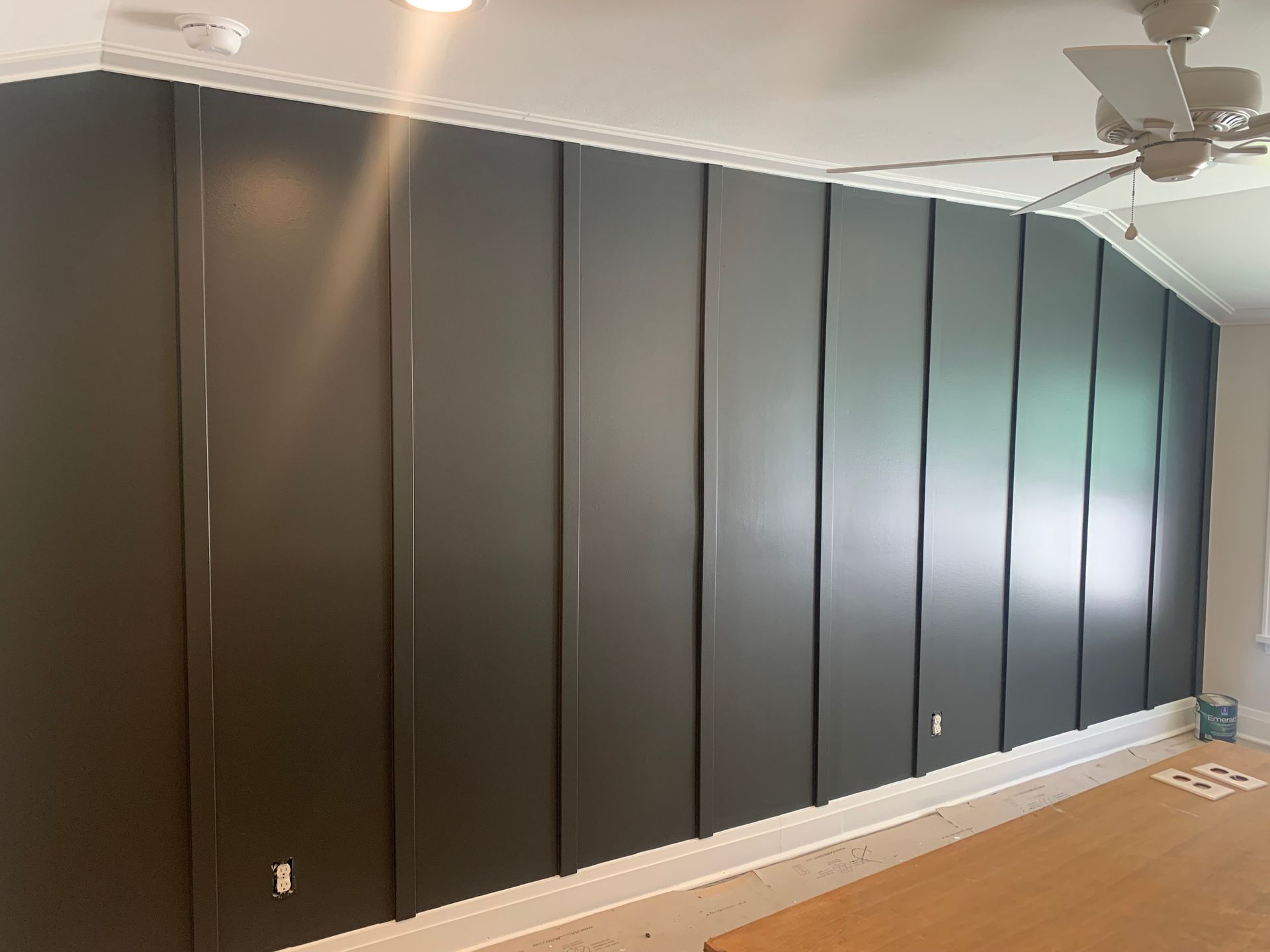 Dark gray panelled accent wall with white trim and a ceiling fan.