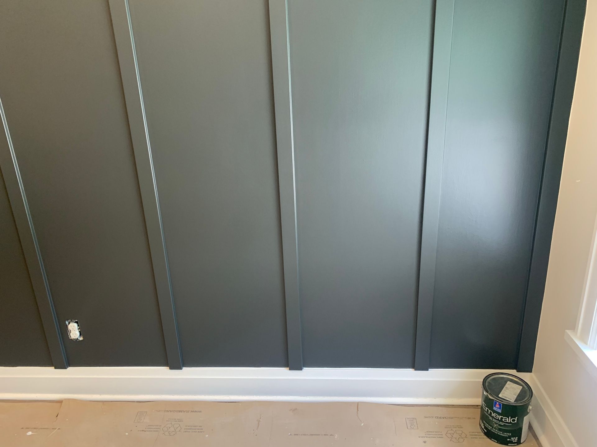 Dark gray board and batten wall, white baseboard, paint can in corner.