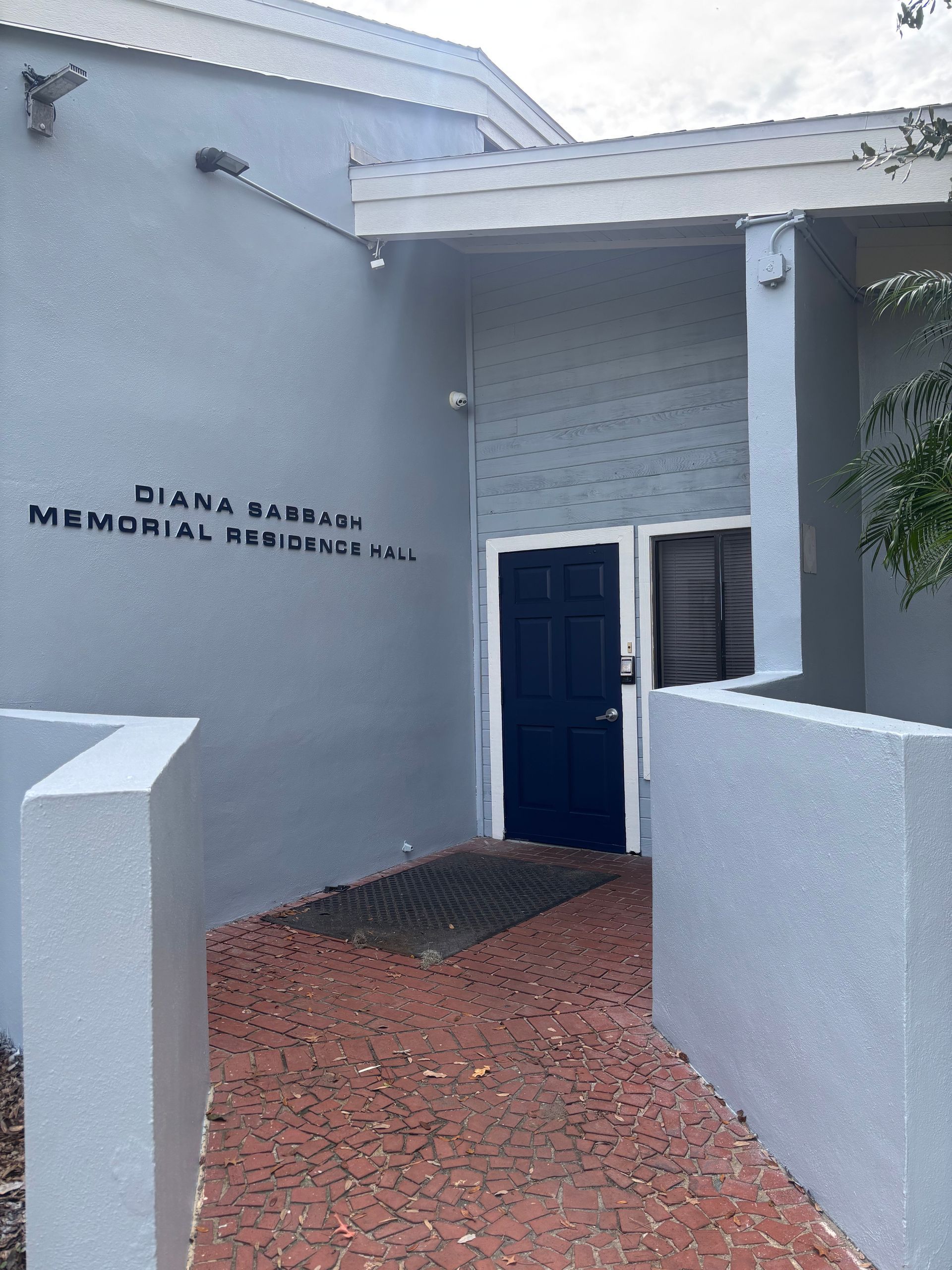 Entrance to Diana Martin Memorial Art Gallery; gray building with blue door, red brick walkway.