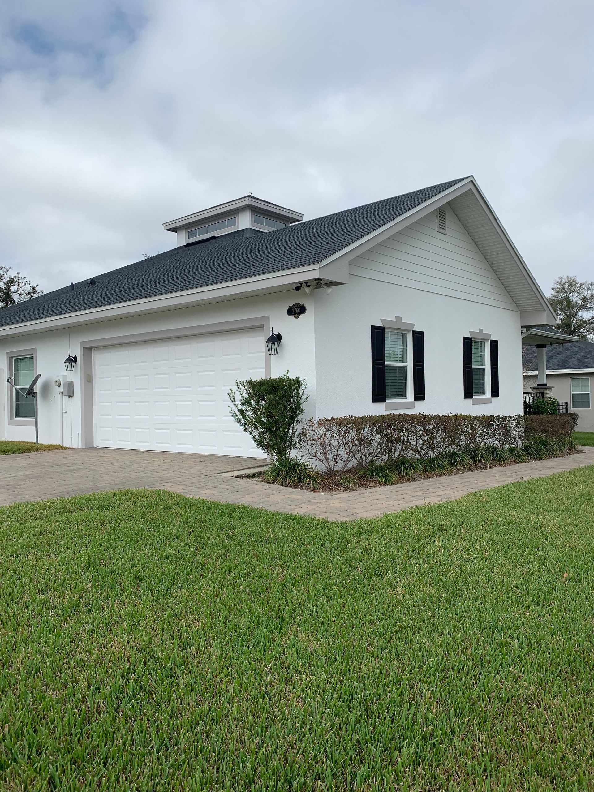 White house with a garage, black shutters, and a stone base. Green grass in front.