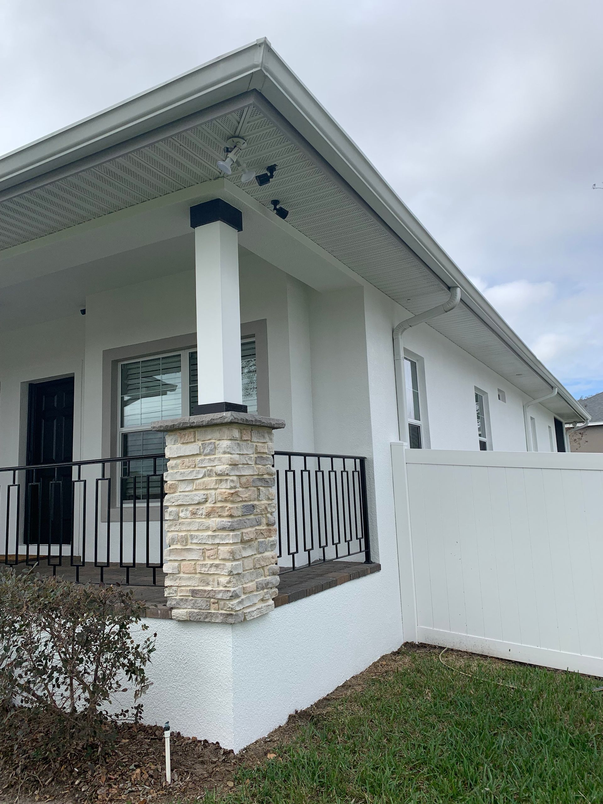 Exterior of a white house with a stone-columned porch, black railings, and white fence.