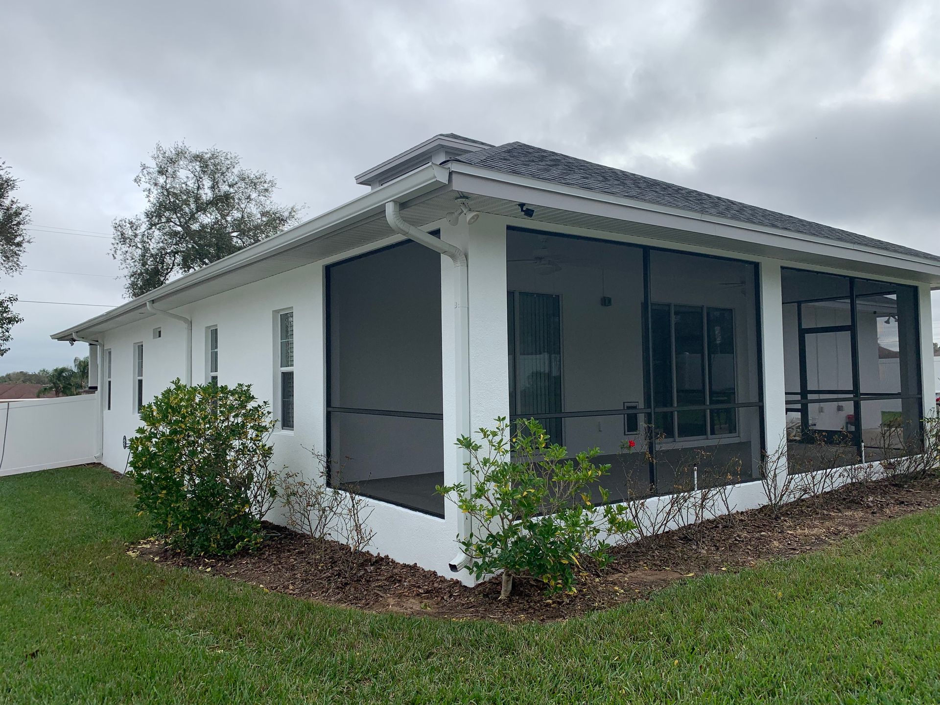 White house with a screened porch, surrounded by green grass and landscaping.