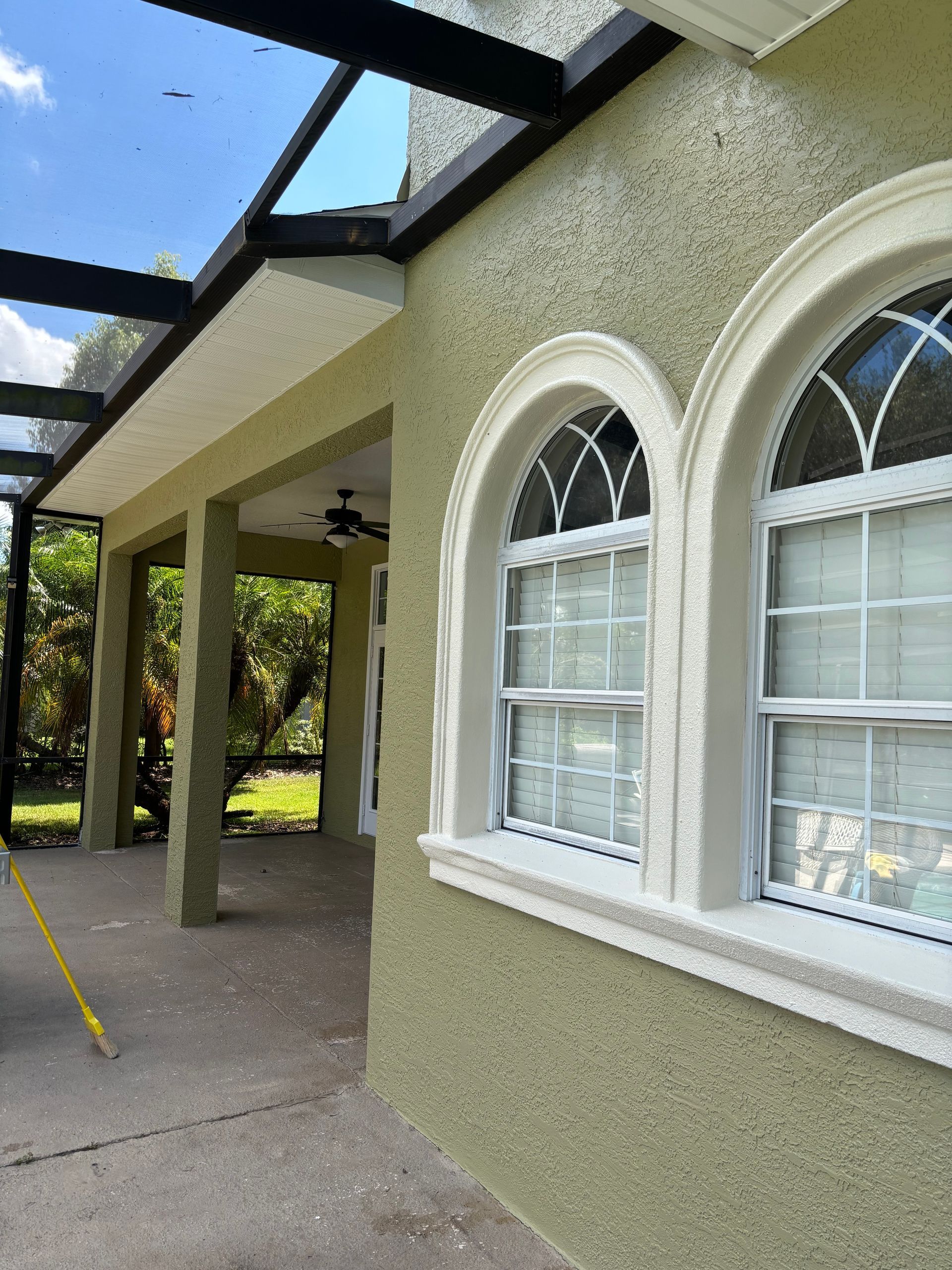 Exterior of a stucco house with arched windows and a covered patio. Olive green walls, white trim, and a sunny day.