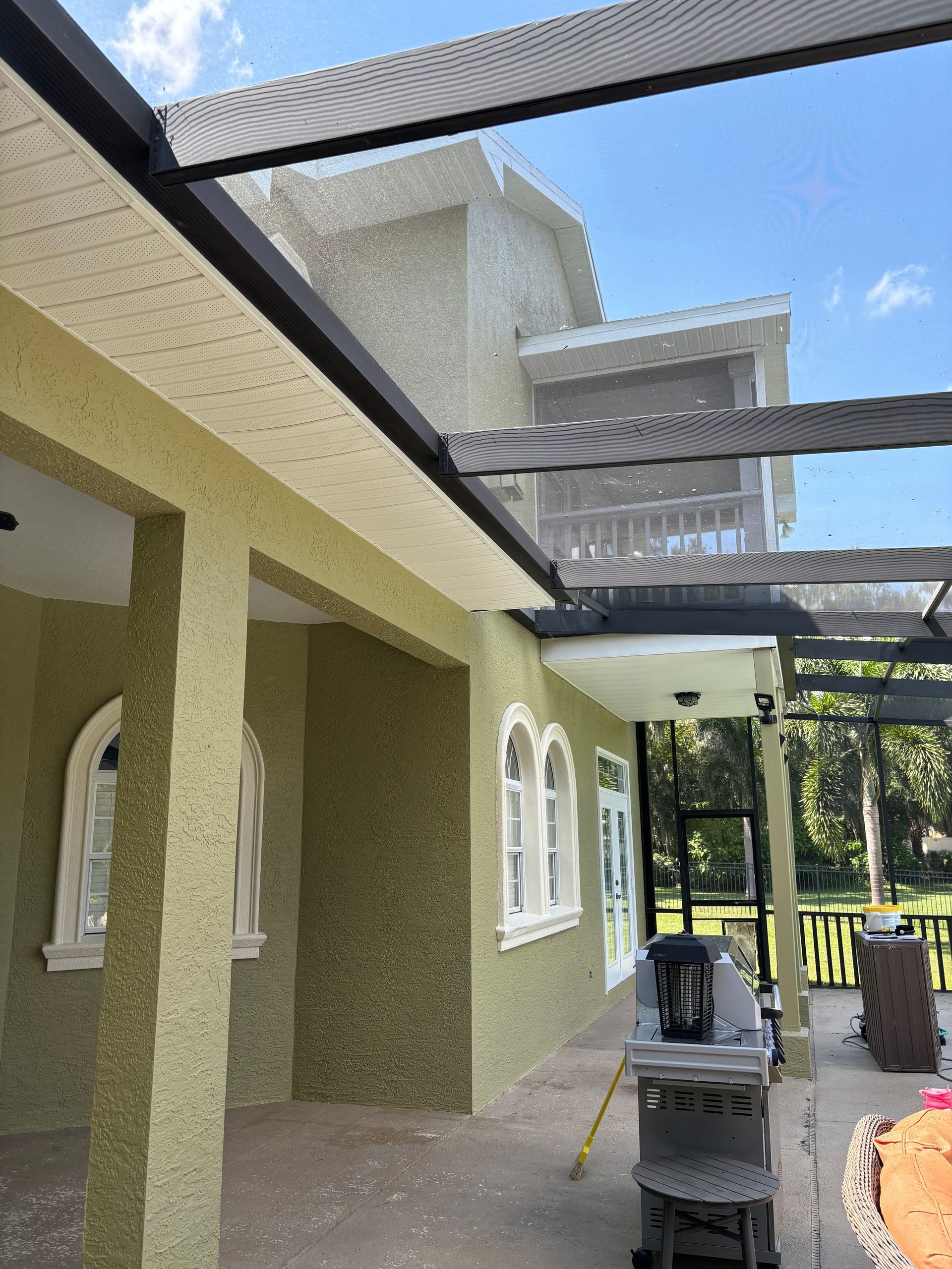 A two-story house with a patio, screened enclosure, and green stucco walls.