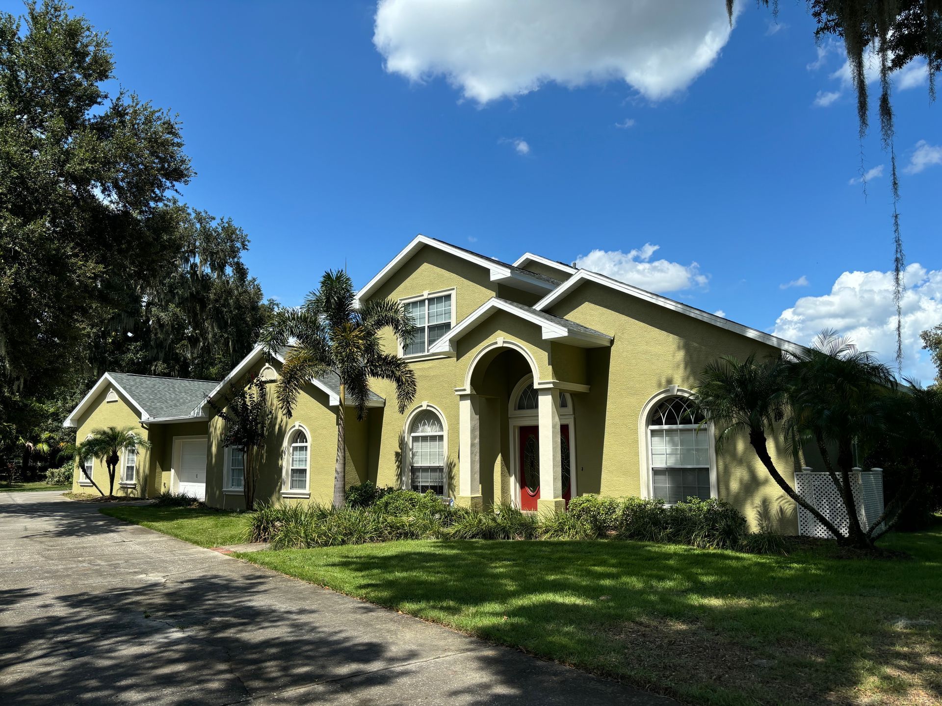 Two-story house with green exterior, white trim, and red front door under a blue sky with clouds.