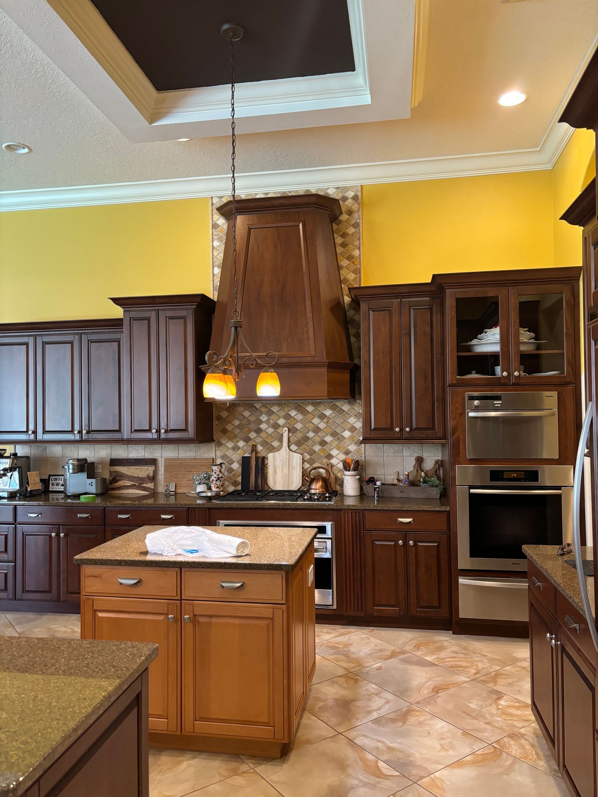 A kitchen with brown cabinets, yellow walls, and an island with granite countertops.