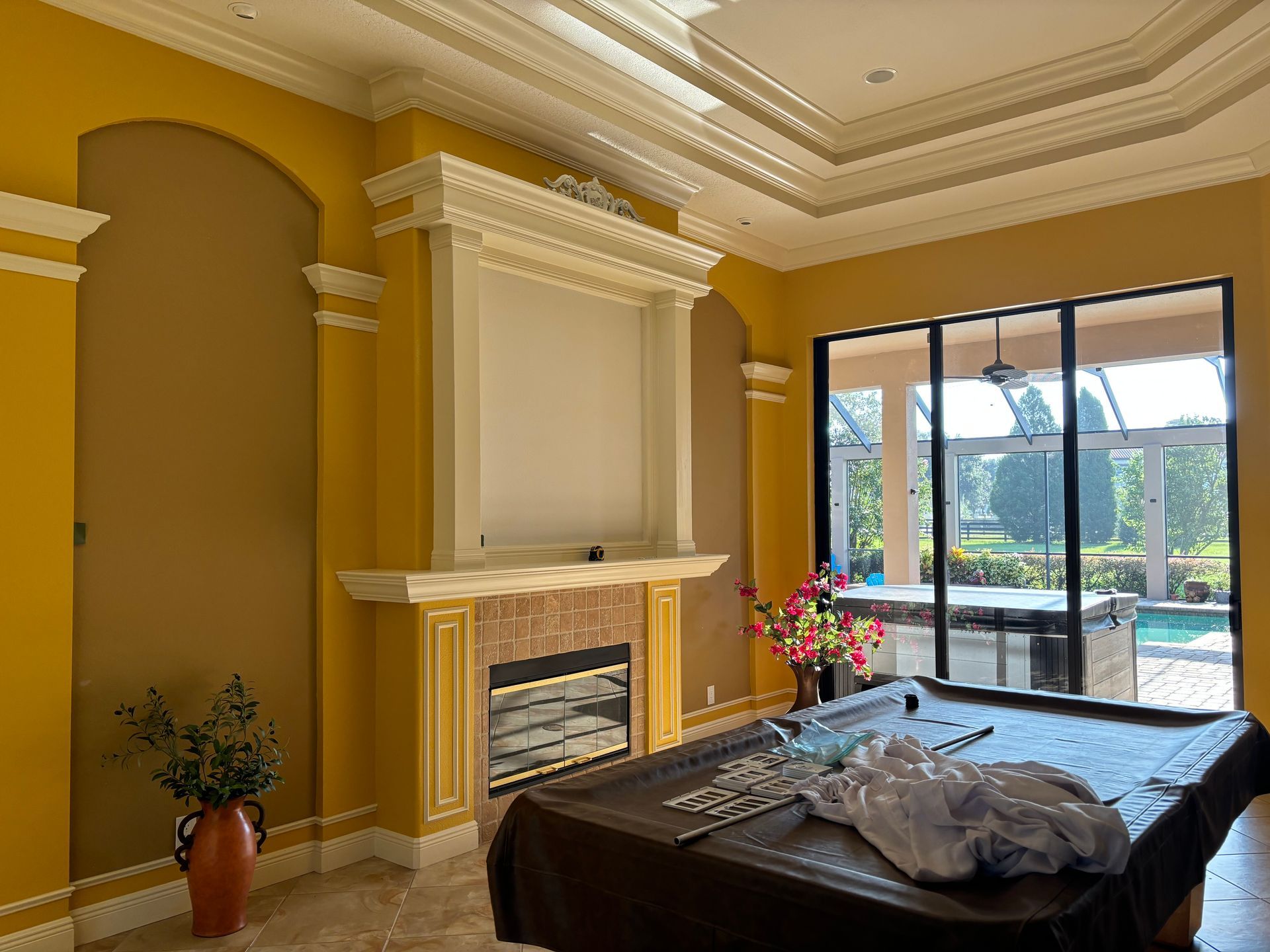 Yellow room with fireplace, arched niches, and a pool table, with view of backyard pool.