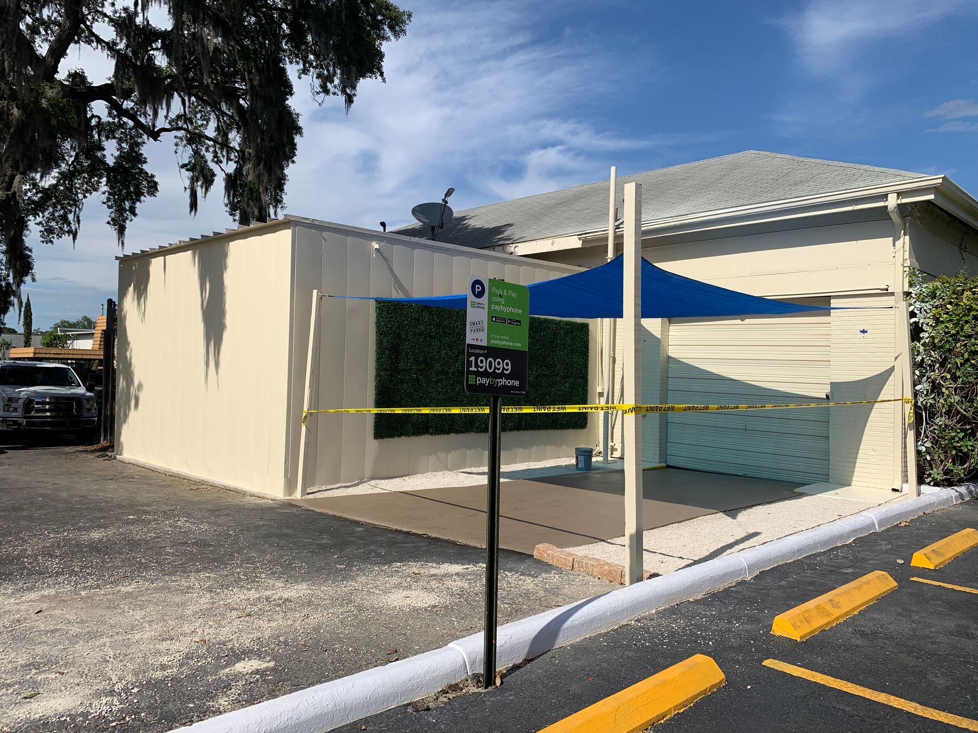 Exterior view of a building with a parking lot. A sign with yellow caution tape. Blue canopy with fake green foliage.