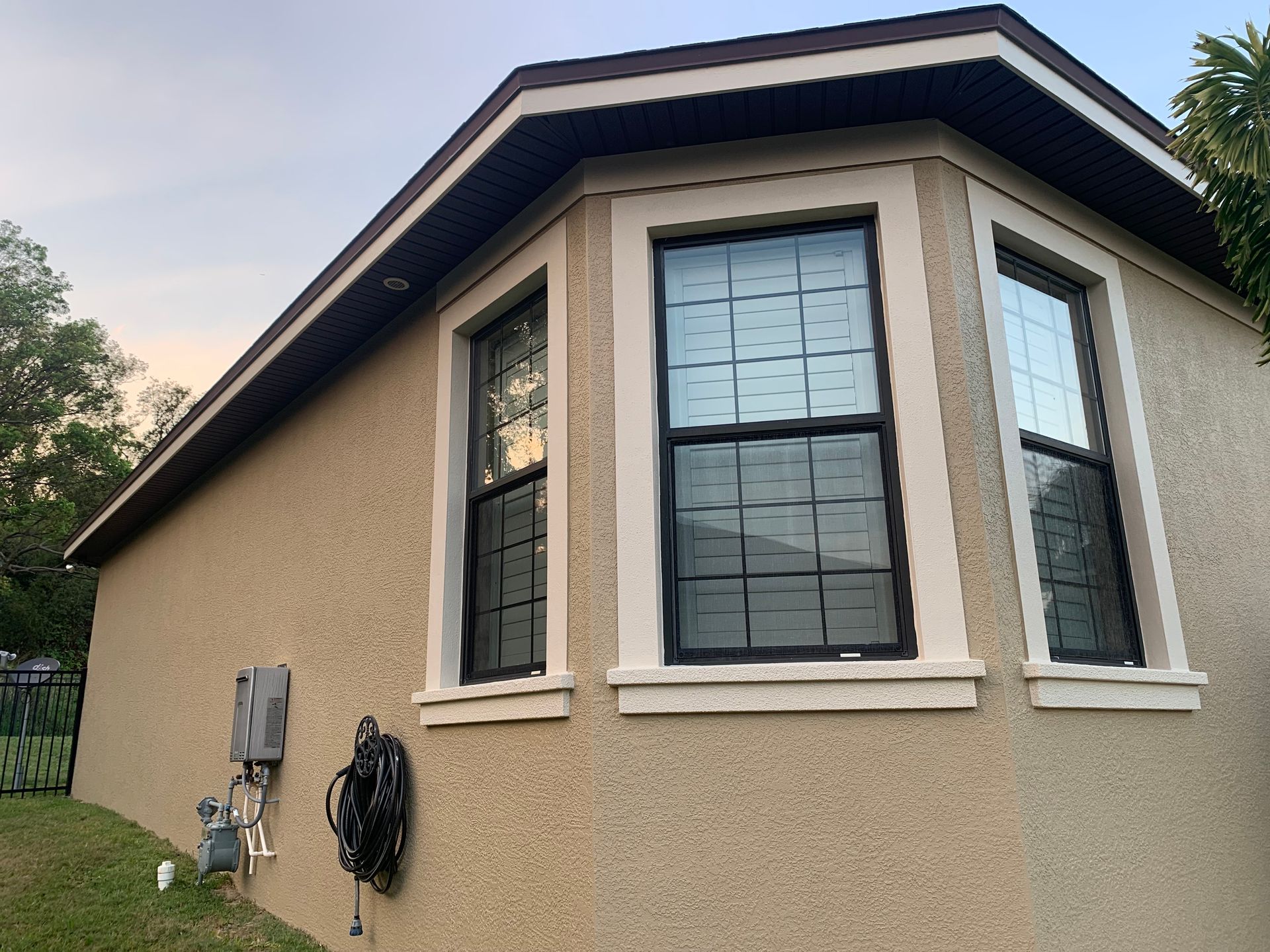 Tan stucco house with bay window, brown trim, and black window frames; dusk setting.