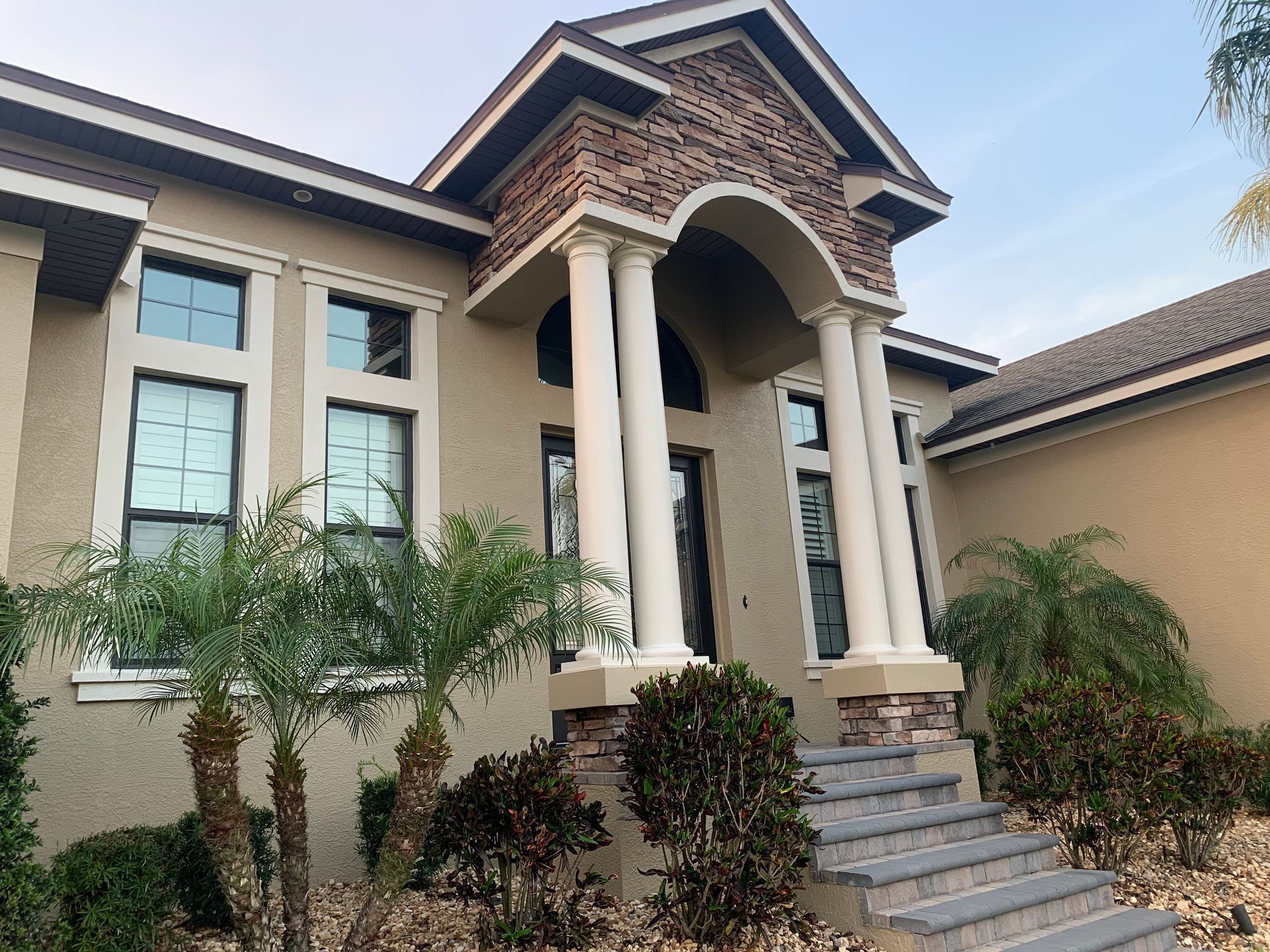 Tan stucco house with columns, stone accents, and steps leading to the front door.