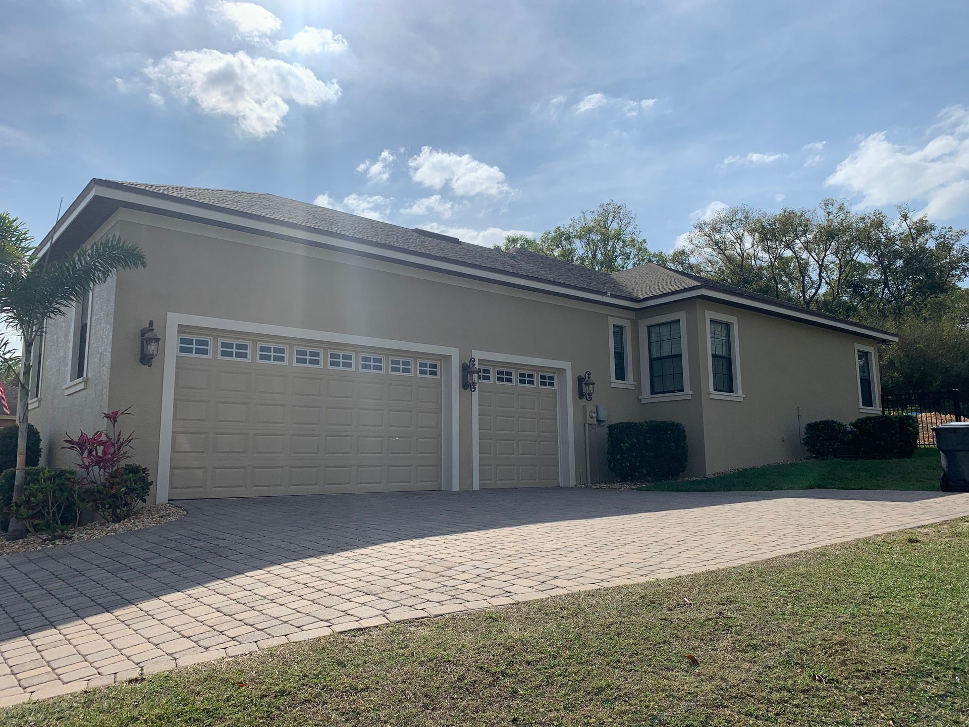 Tan stucco house with brick driveway, two-car garage, and cloudy sky.