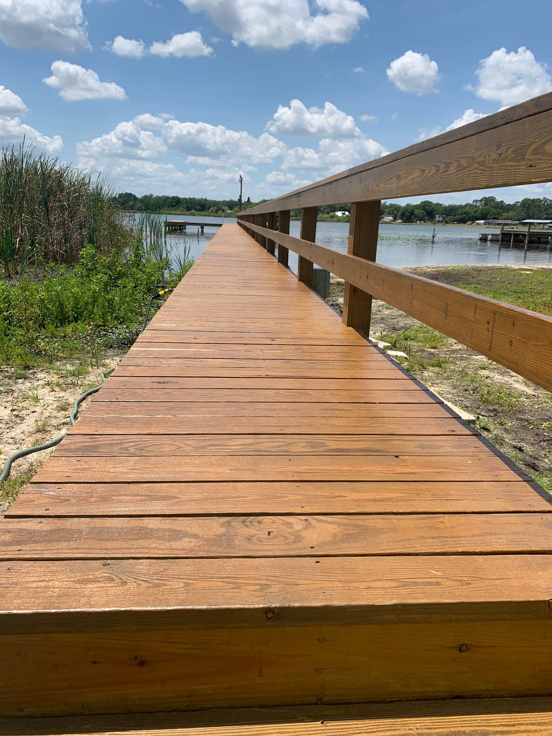 Wooden boardwalk extends to a lake, with railing and blue sky.