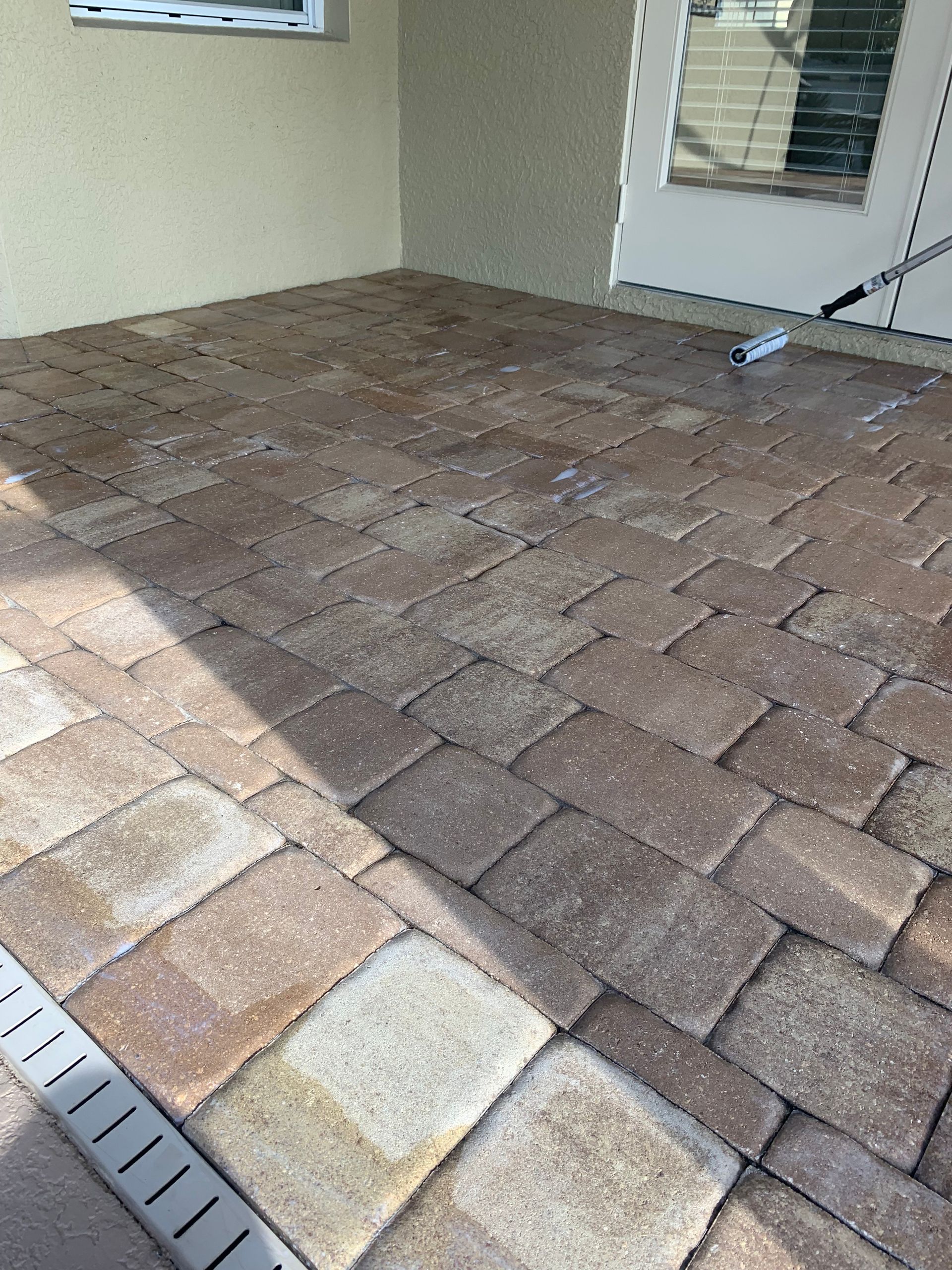 Brick patio being cleaned; beige and brown pavers next to a cream stucco wall.