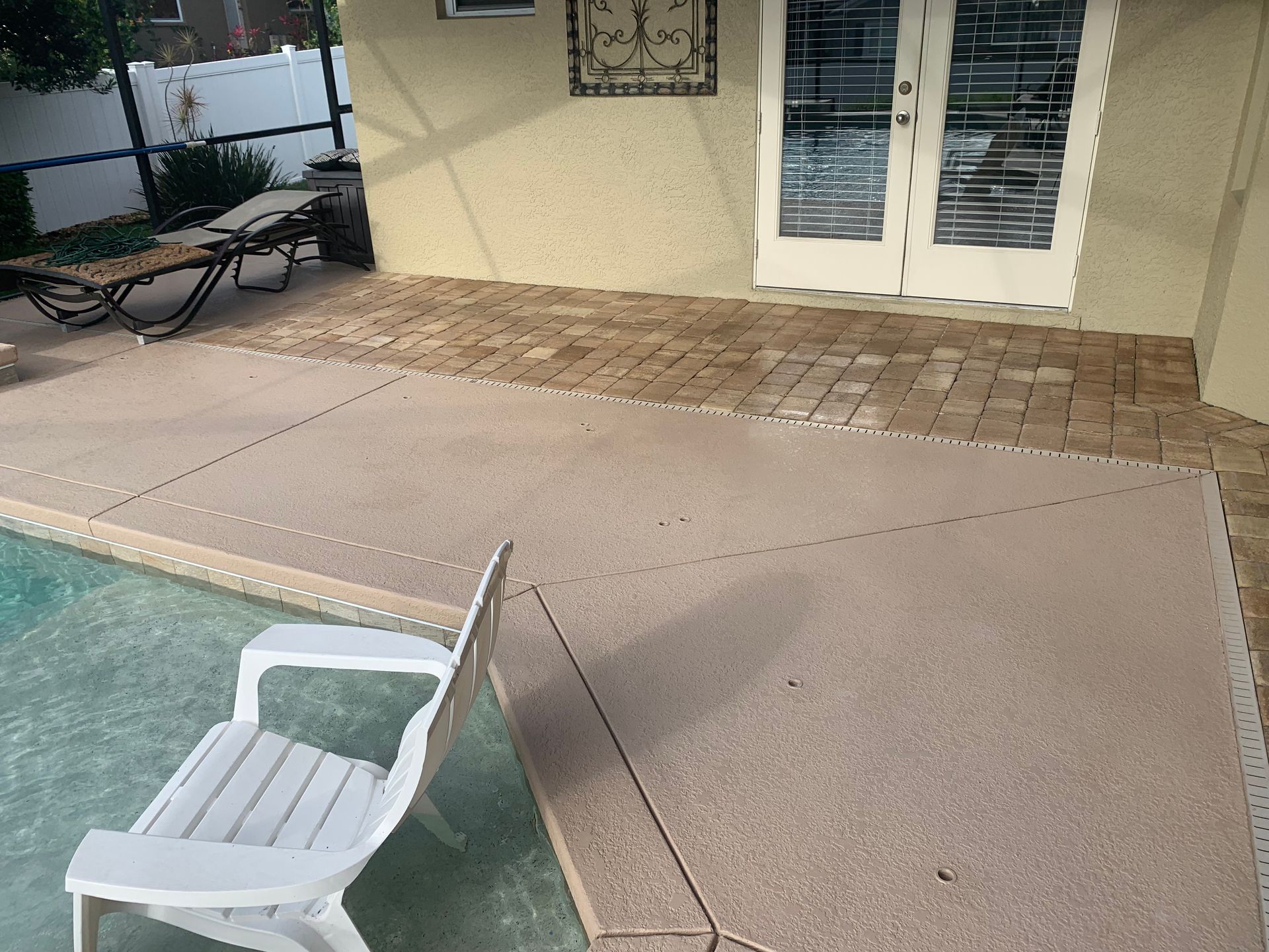 Patio with pool, beige concrete, white chair, and French doors.