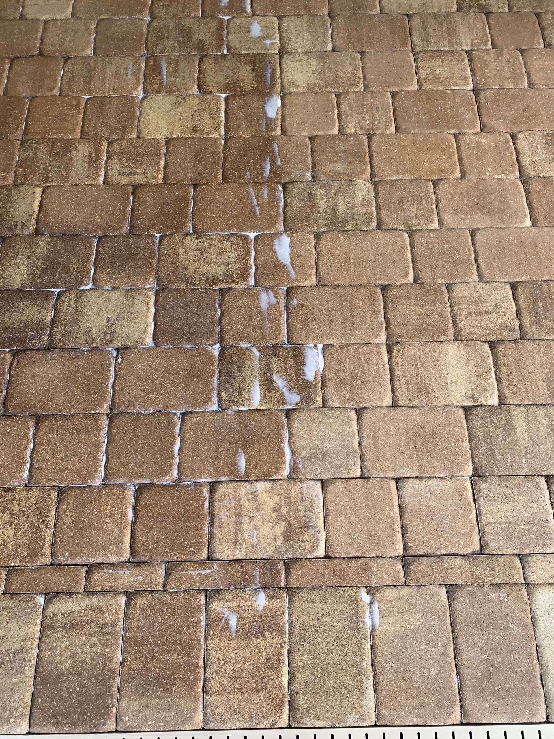 Pavers being cleaned, showing a stark contrast between dirty and clean sections, in a paved outdoor area.