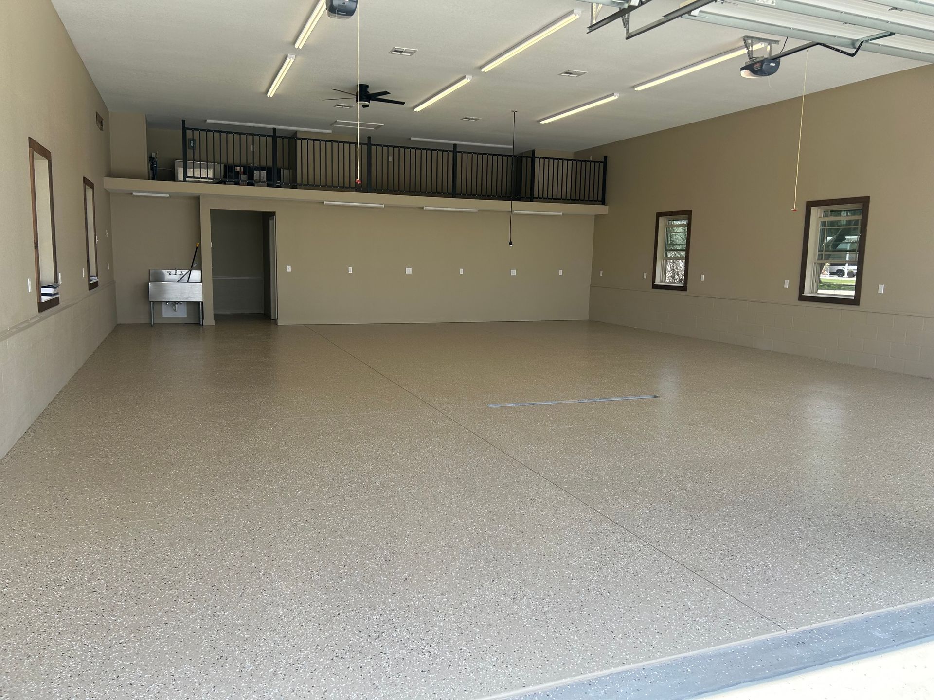 Spacious garage with tan walls, a polished speckled floor, and a small storage loft area.
