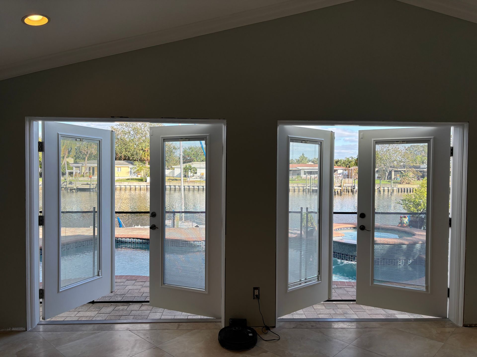 Two white French doors open to a waterfront view, casting striped shadows inside the room.