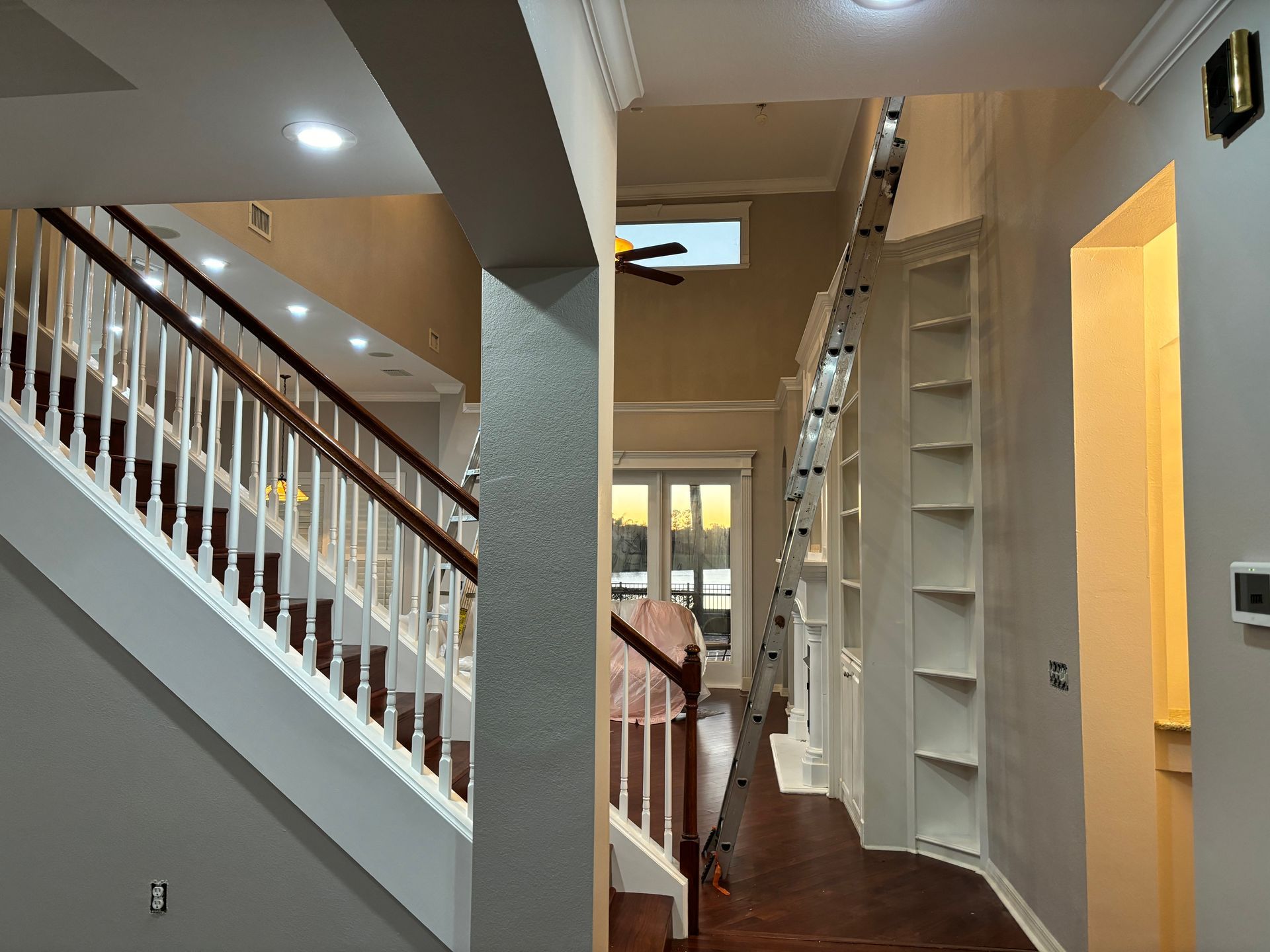 Interior view of a house with staircase, built-in shelves, and open spaces. Sunlight and warm colors.