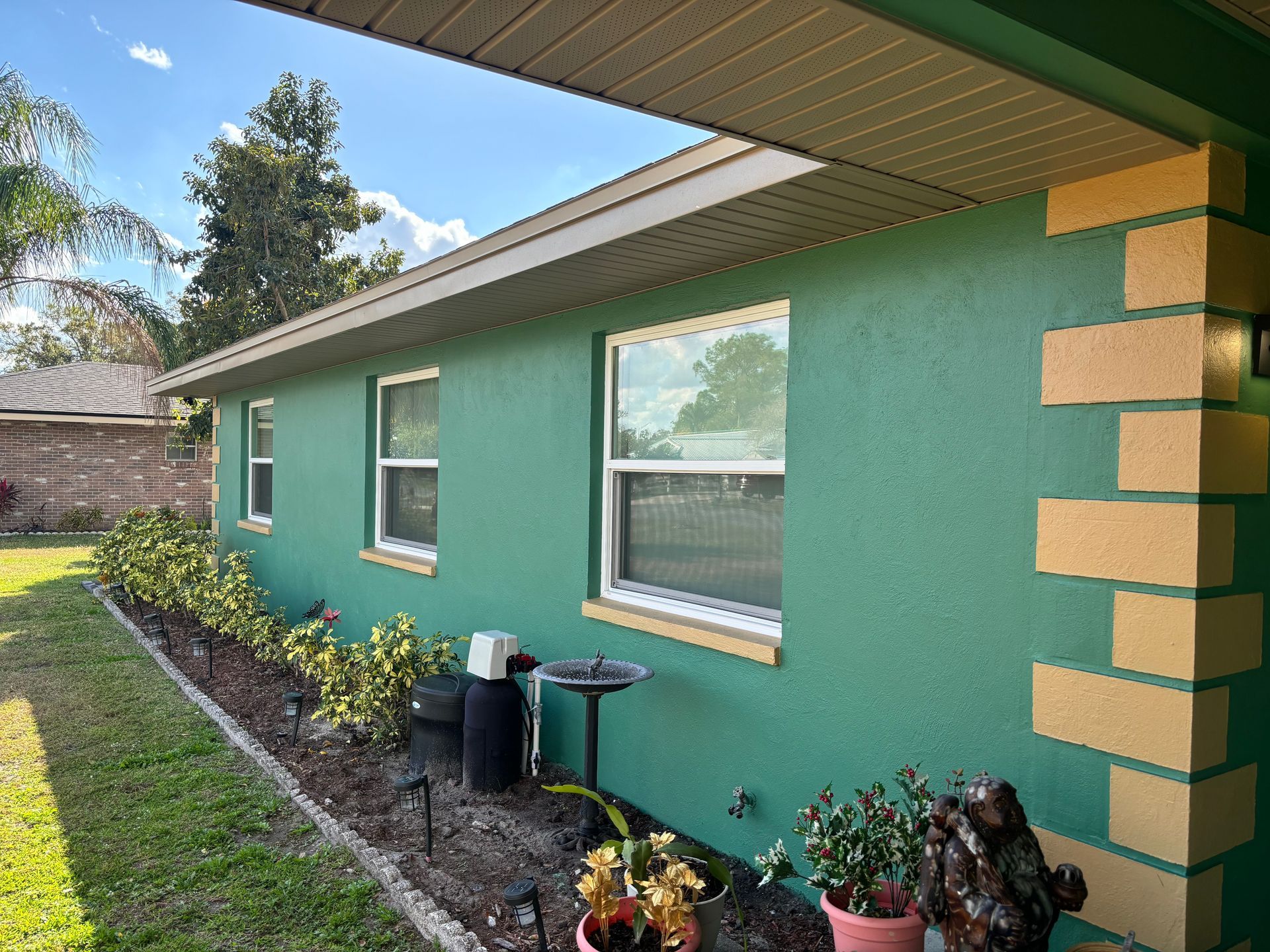 Green house exterior with beige trim, windows, and accent columns; small garden in front.