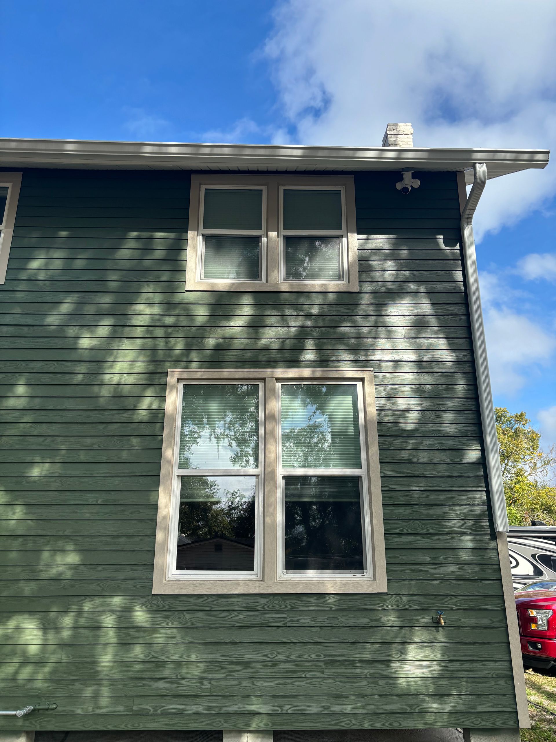 Green wooden building with two sets of windows, under a blue sky.
