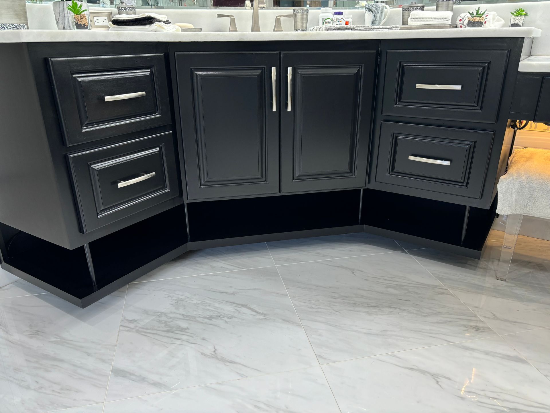 Black bathroom vanity with drawers and doors, on light gray tiled floor.