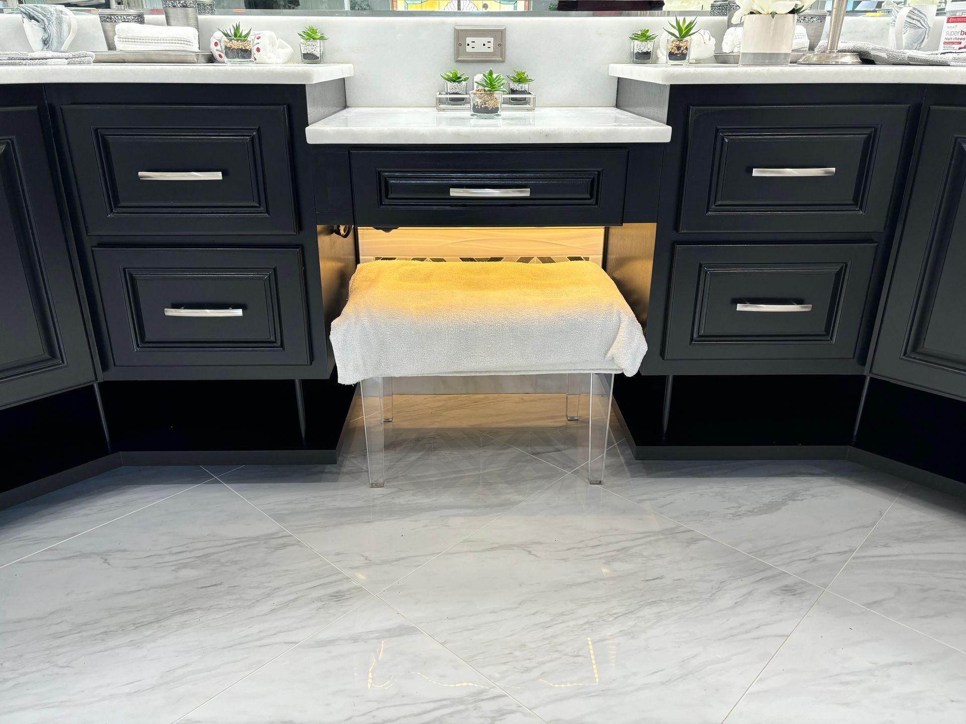 Black vanity with marble countertop, built-in illuminated space for a clear stool, bathroom setting.