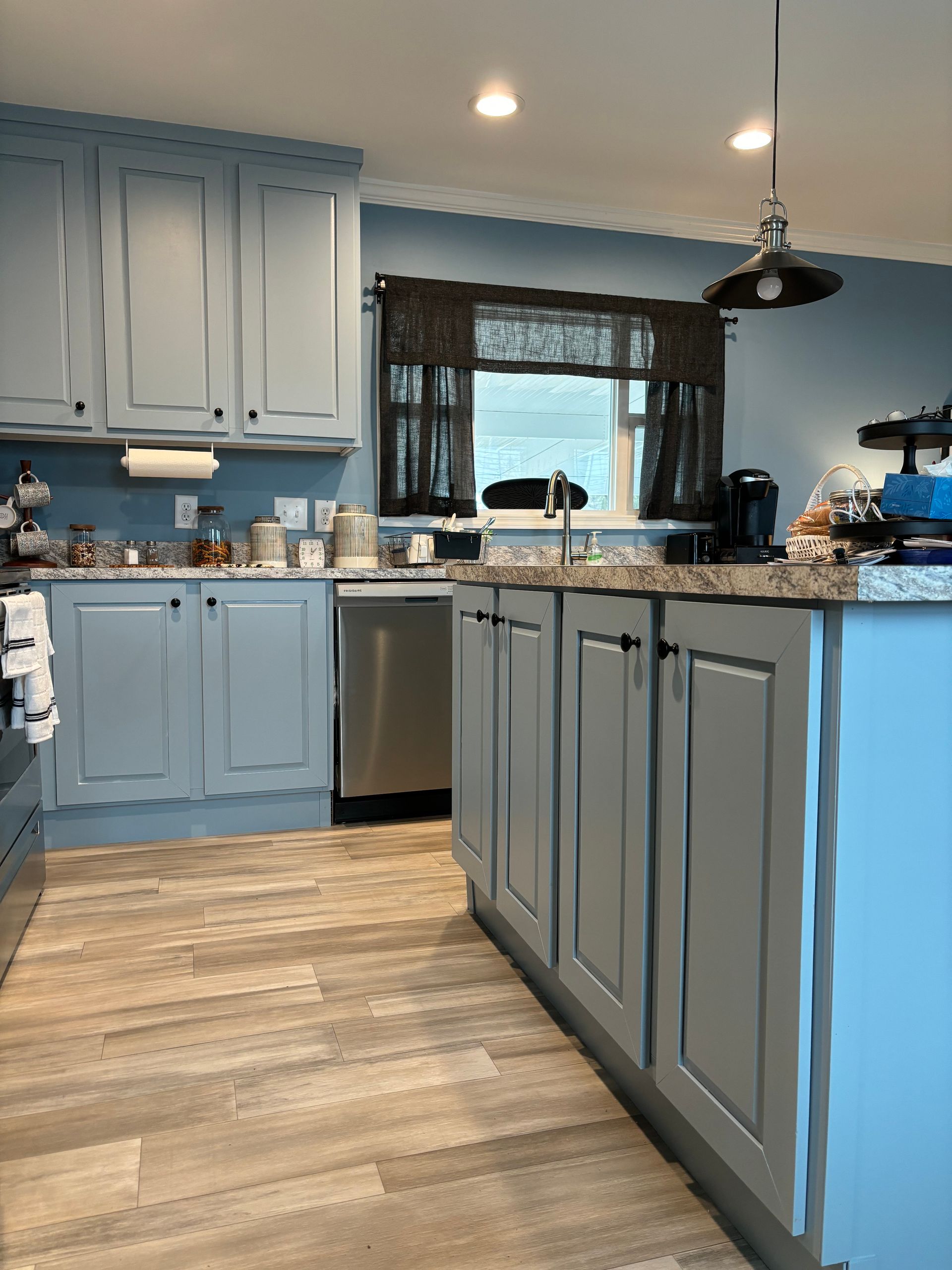 Light blue kitchen with wooden floor, stainless steel appliances, and dark countertop.