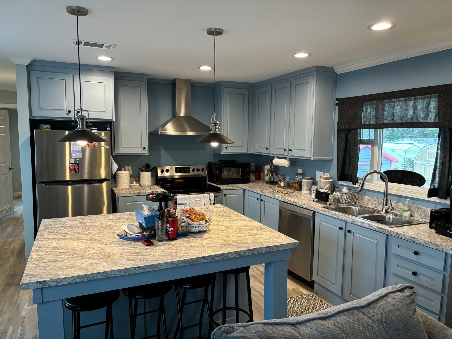 Light blue kitchen with an island, stainless steel appliances, and a window.