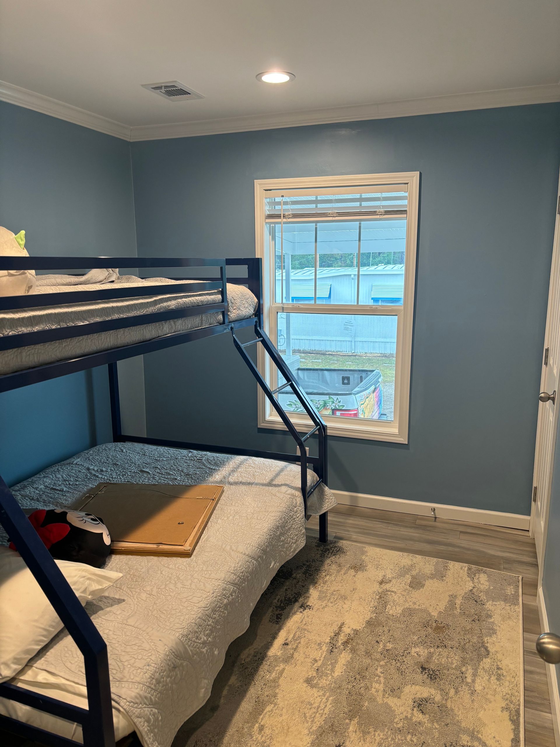 Blue bedroom with bunk beds, a window, and a rug on a gray floor.
