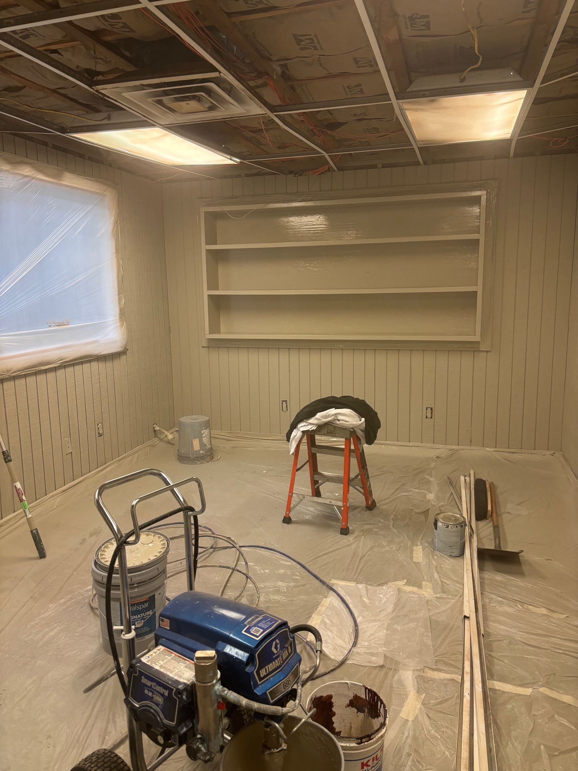 Room being painted; shelves and walls are beige, painting equipment in foreground.