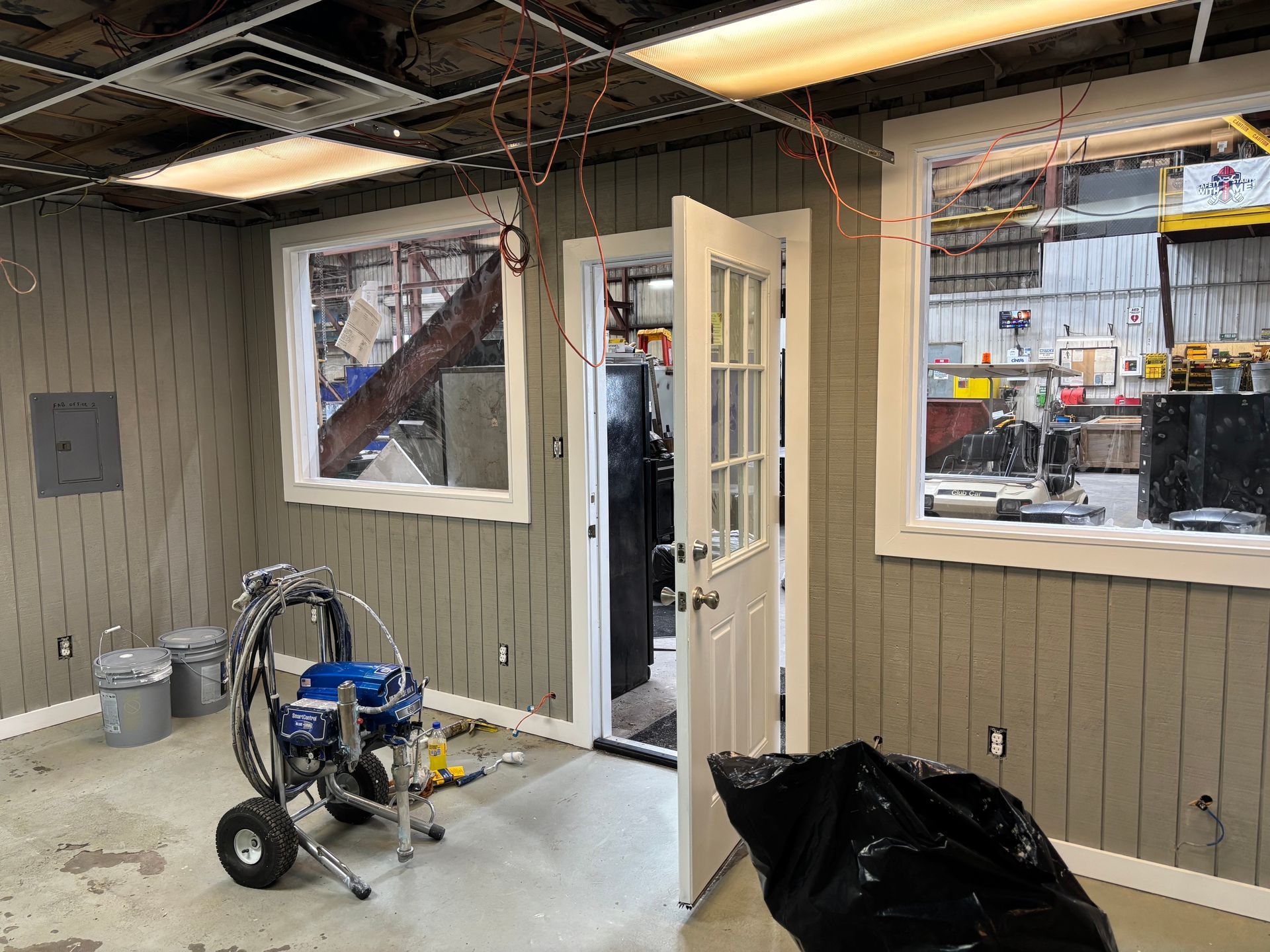 Interior view of a room under construction with windows, a door, and painting equipment.