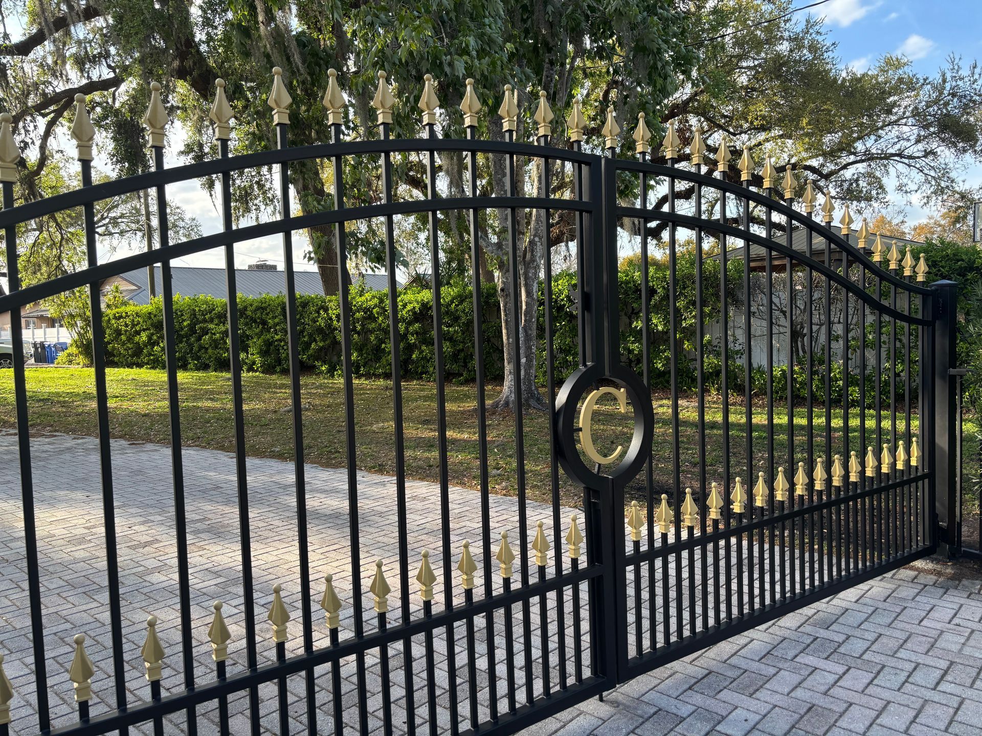 Black wrought iron gate with gold accents, blocking driveway. 