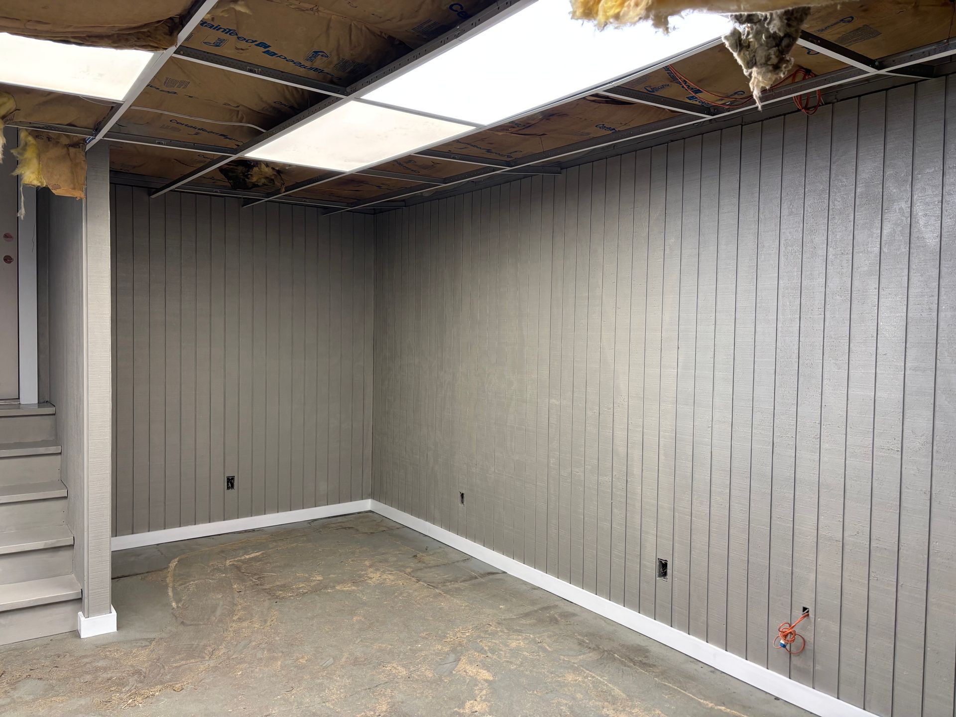 Empty room with gray panel walls, white trim, exposed ceiling, and bare concrete floor.