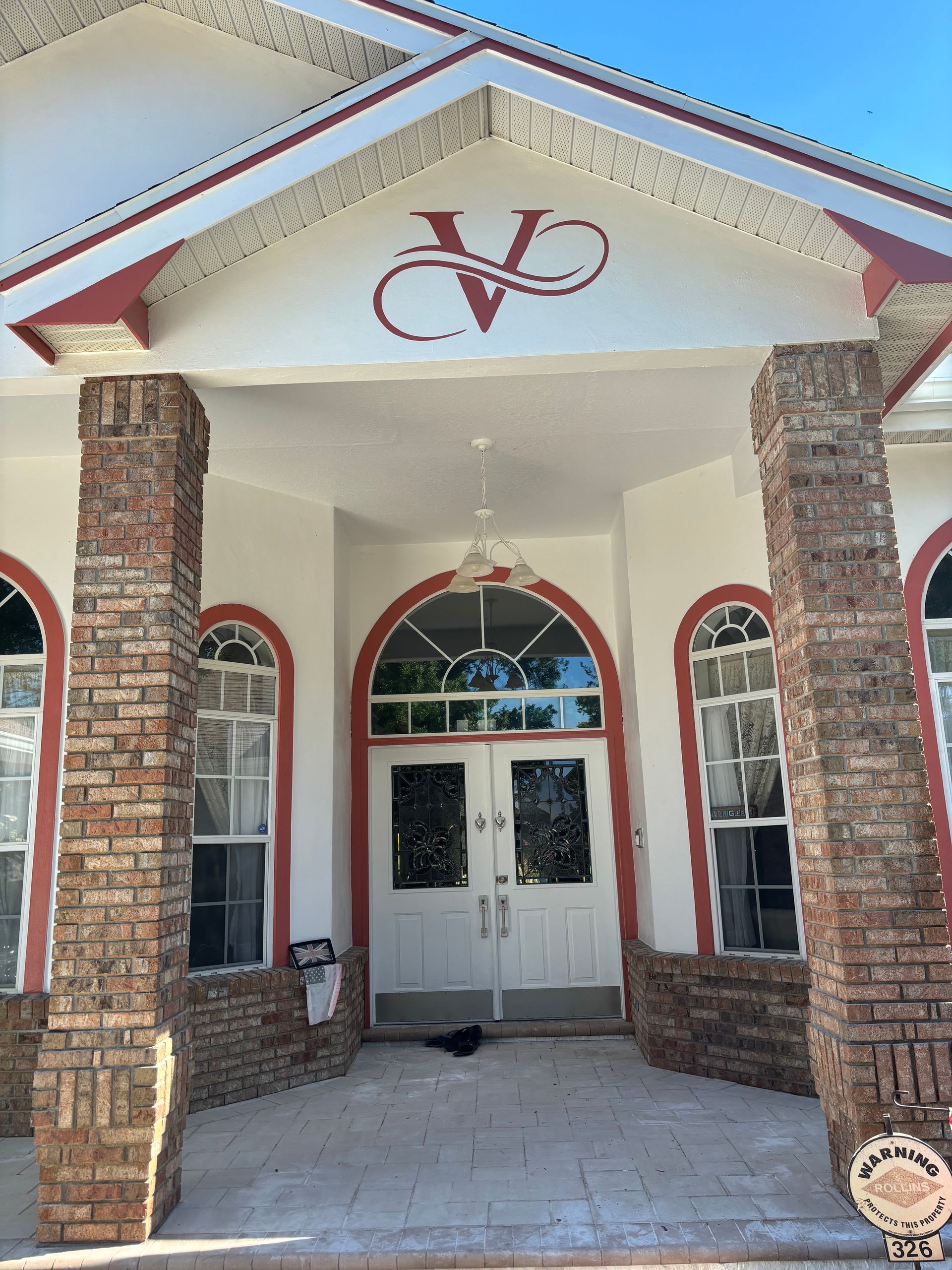 Exterior of a building with white walls, red trim, brick columns, and a double-door entrance under the letter 