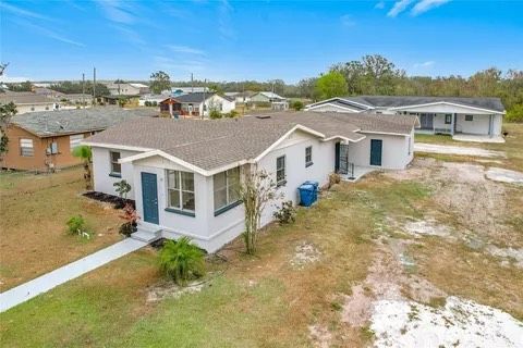 A light gray house with a brown roof and blue doors, in a suburban area on a sunny day.