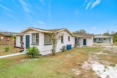 Single-story white house with blue door and trim, on a grassy lot under a blue sky.