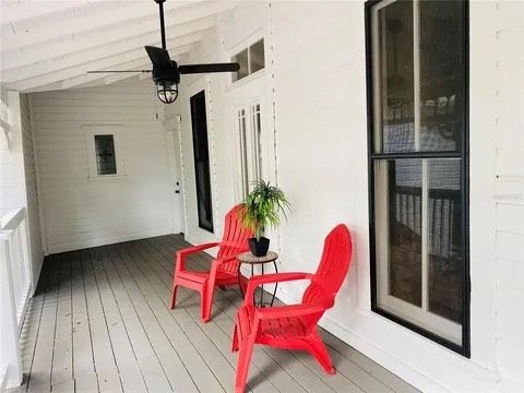 A porch with red chairs, a small table, and a hanging fan. White walls, gray floor, and black windows.