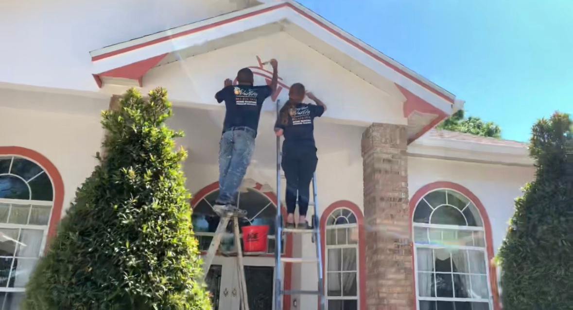 A man and a woman are painting the roof of a house.