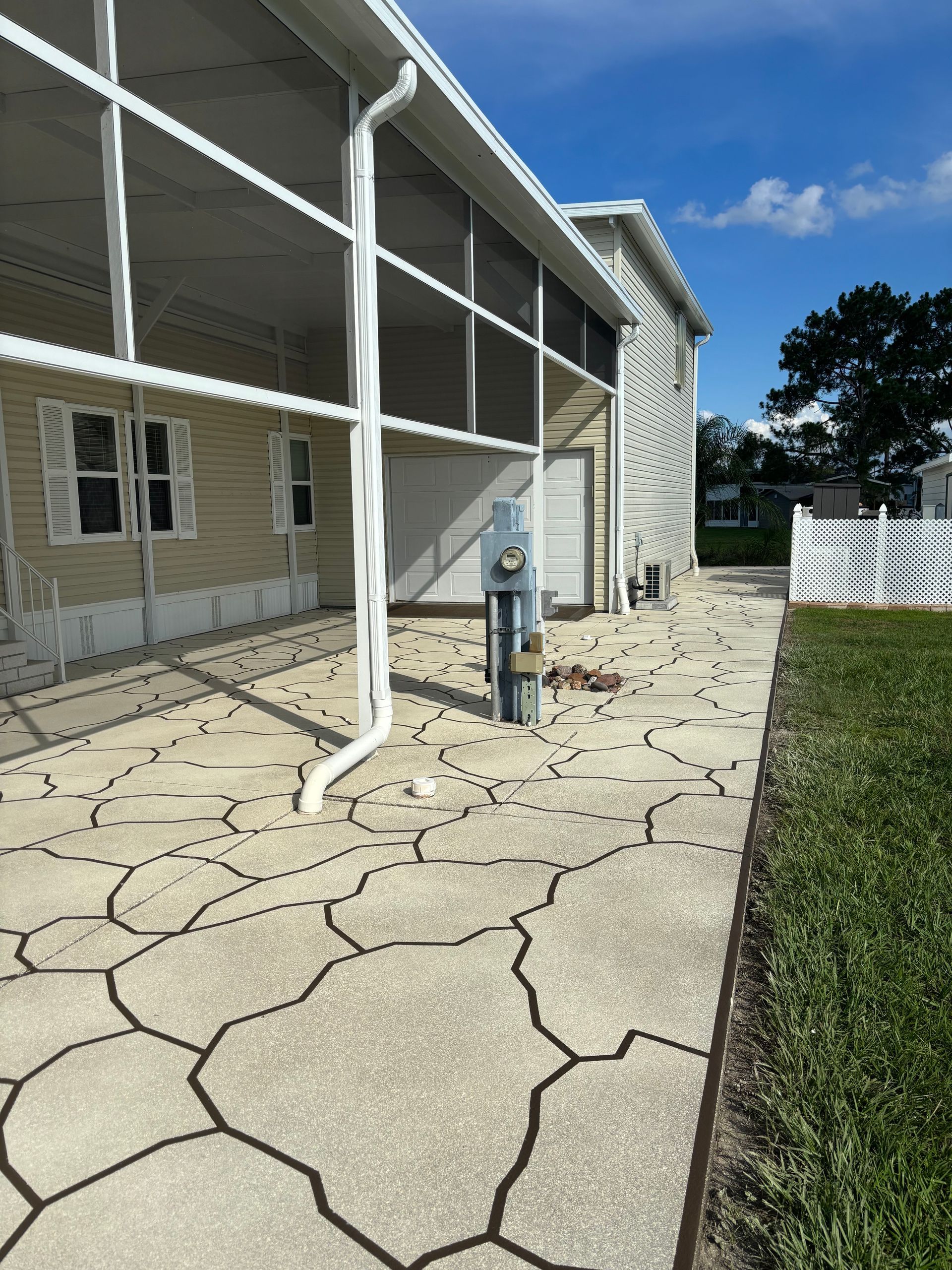 Patio with patterned concrete, white screen enclosure, and a house with beige siding under a blue sky.