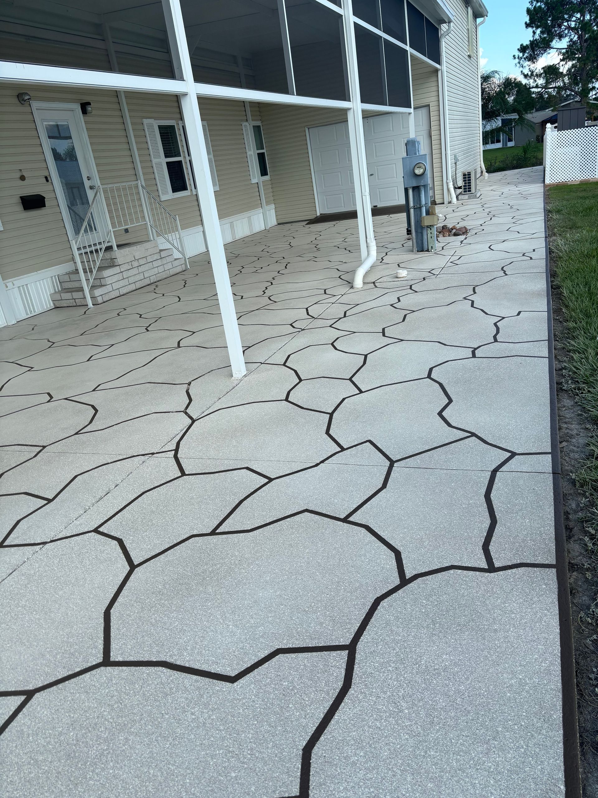 Concrete walkway with dark grout lines, next to a building with a screened porch.
