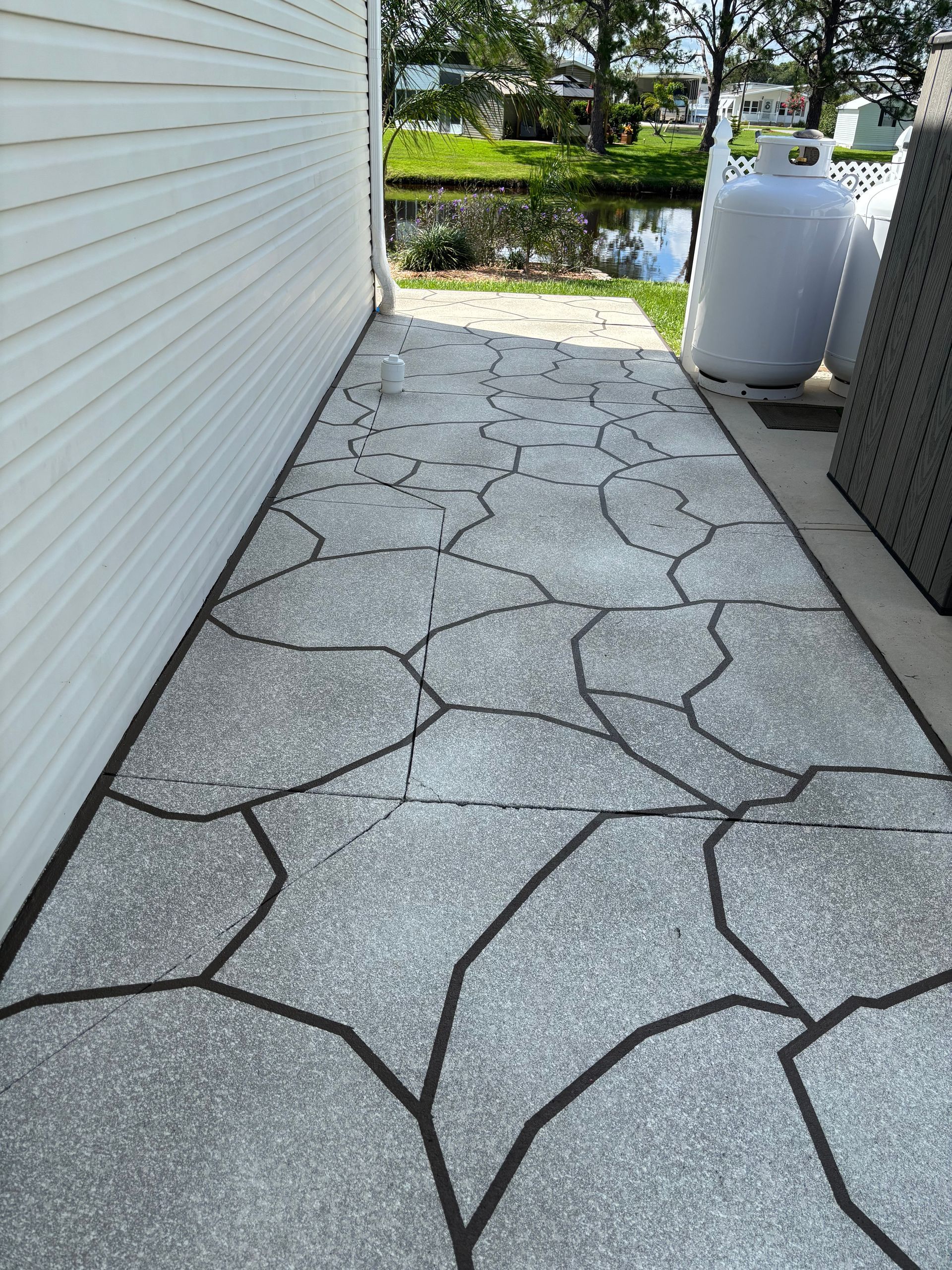 A narrow concrete walkway with a stone-like design runs alongside a white building, leading to a small pond.